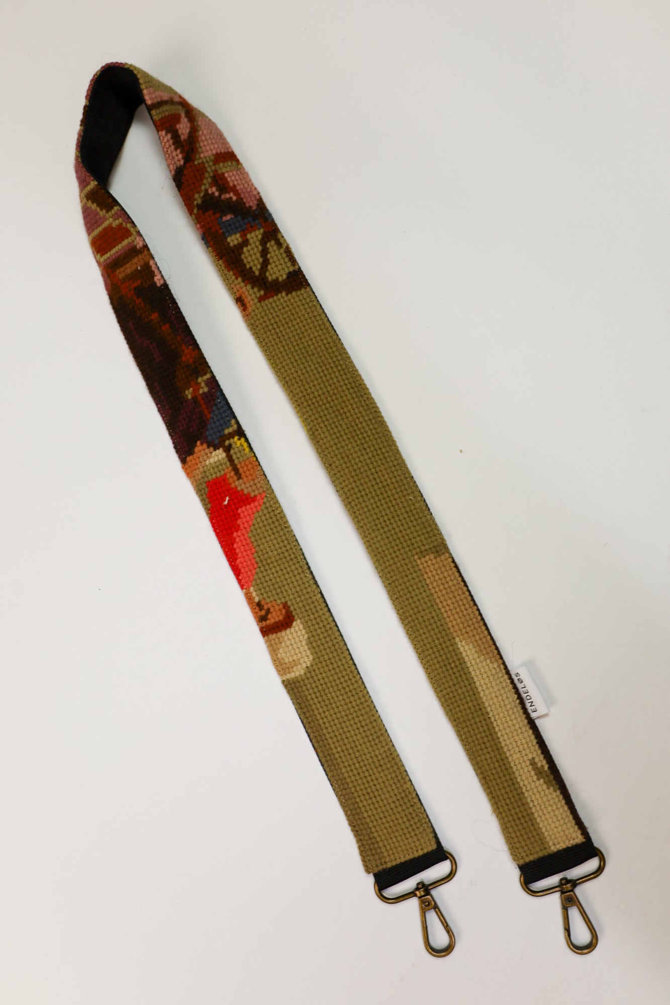 Detail van een strap met een geborduurd kunstwerk in natuurlijke tinten en subtiele accenten van roze en paars, gemaakt van hergebruikte materialen