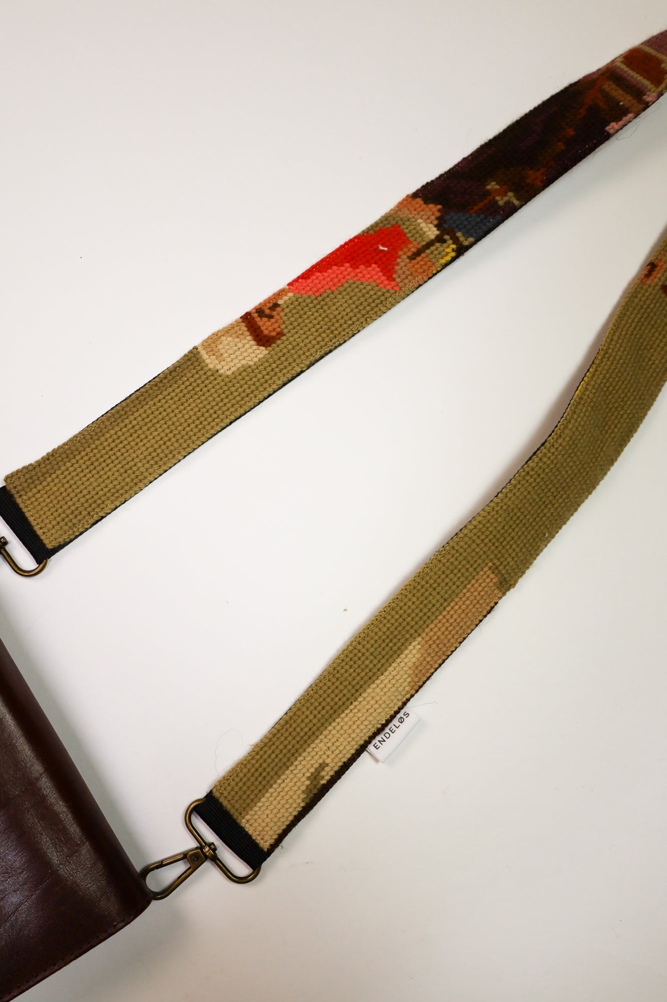 Strap gemaakt van een kleurrijk geborduurd schilderij in natuurlijke tinten met accenten van roze en paars, perfect voor het verfraaien van je tas, telefoon of camera.