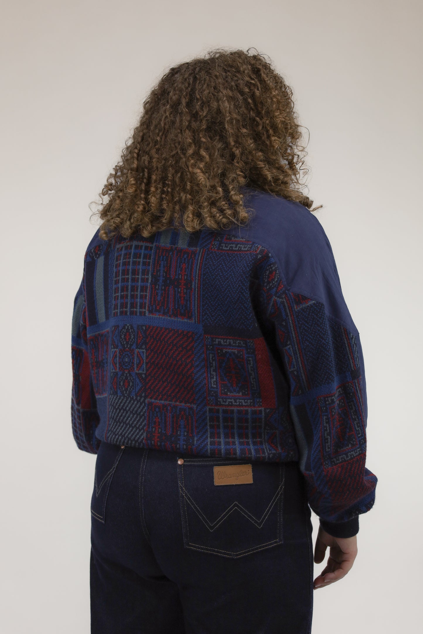 Achteraanzicht van model met blauw-rood vintage bomberjack met gebreide details.