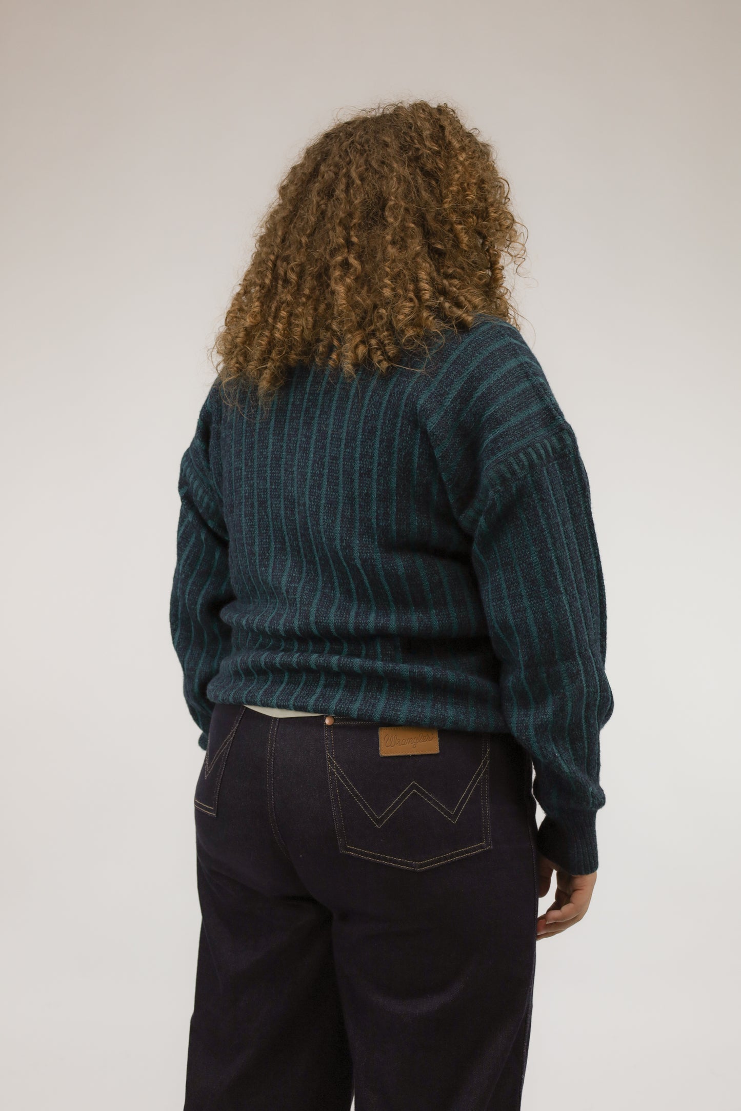 Achteraanzicht van model met ruimvallende vintage trui in groen-blauwe strepen.