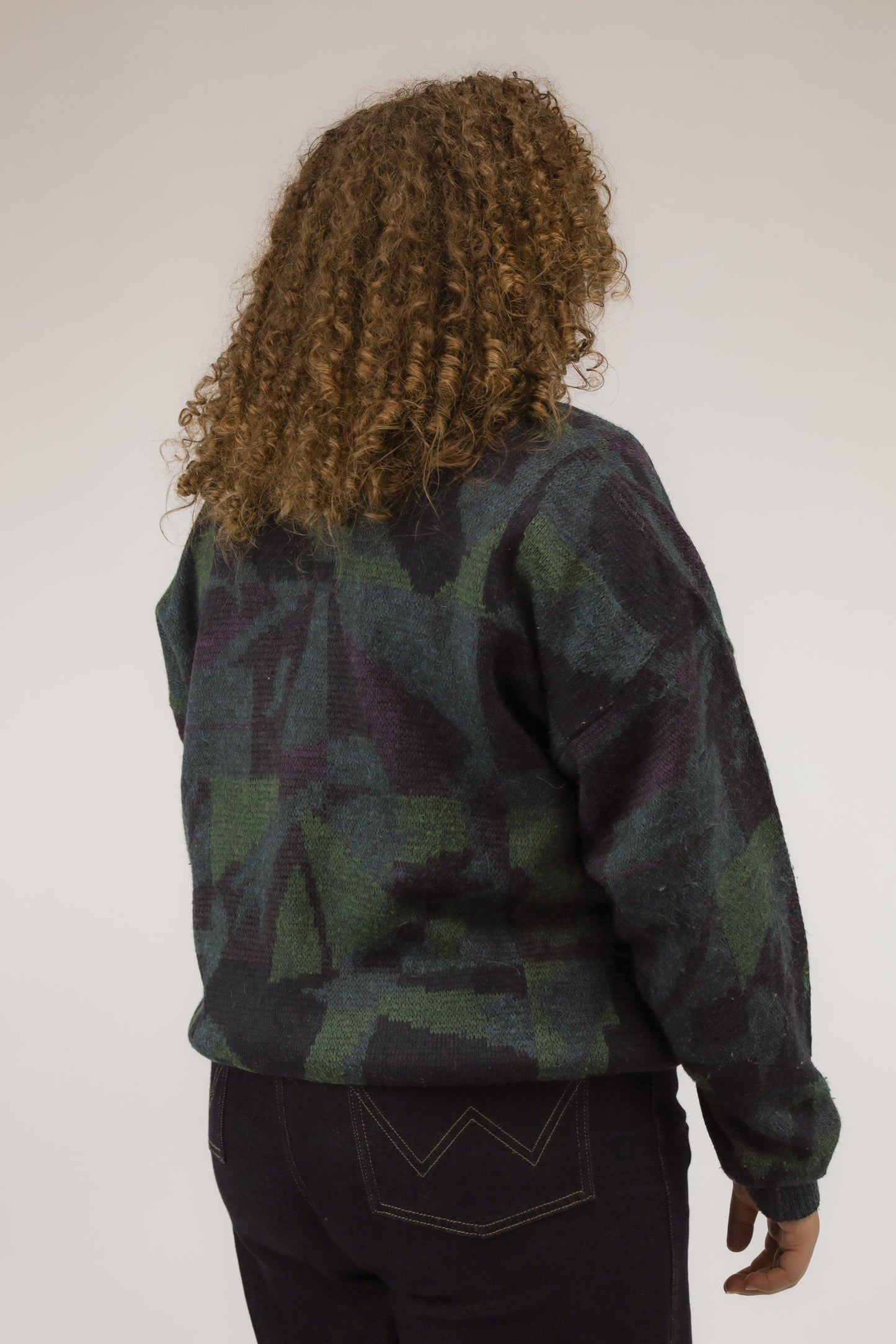 Model van achteren met vintage oversized trui in blauw- en groentinten – grafisch dessin over de rug