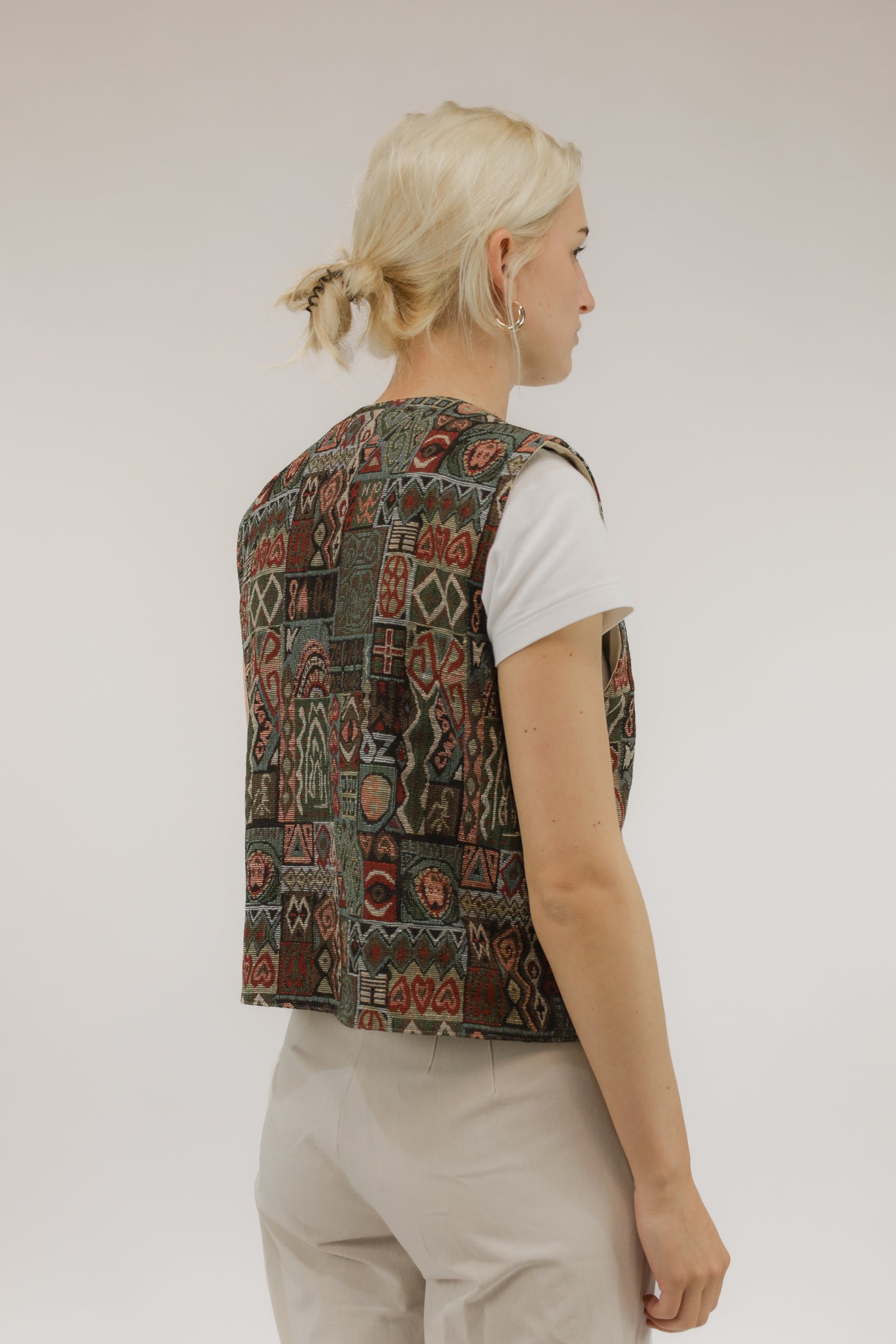Model van achteren met vintage jacquard geweven gilet – rijke textuur en aardse kleurcombinatie zichtbaar.