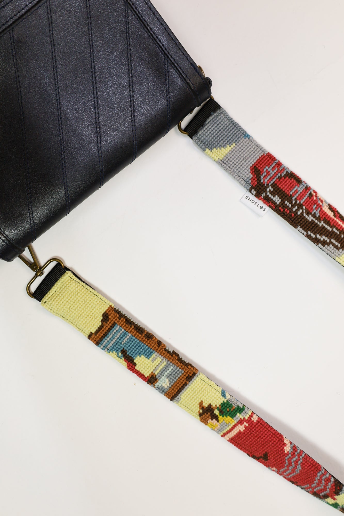 Detail van een strap met een kunstzinnig geborduurd motief in zachte kleuren, gemaakt van hergebruikte materialen voor een unieke uitstraling.