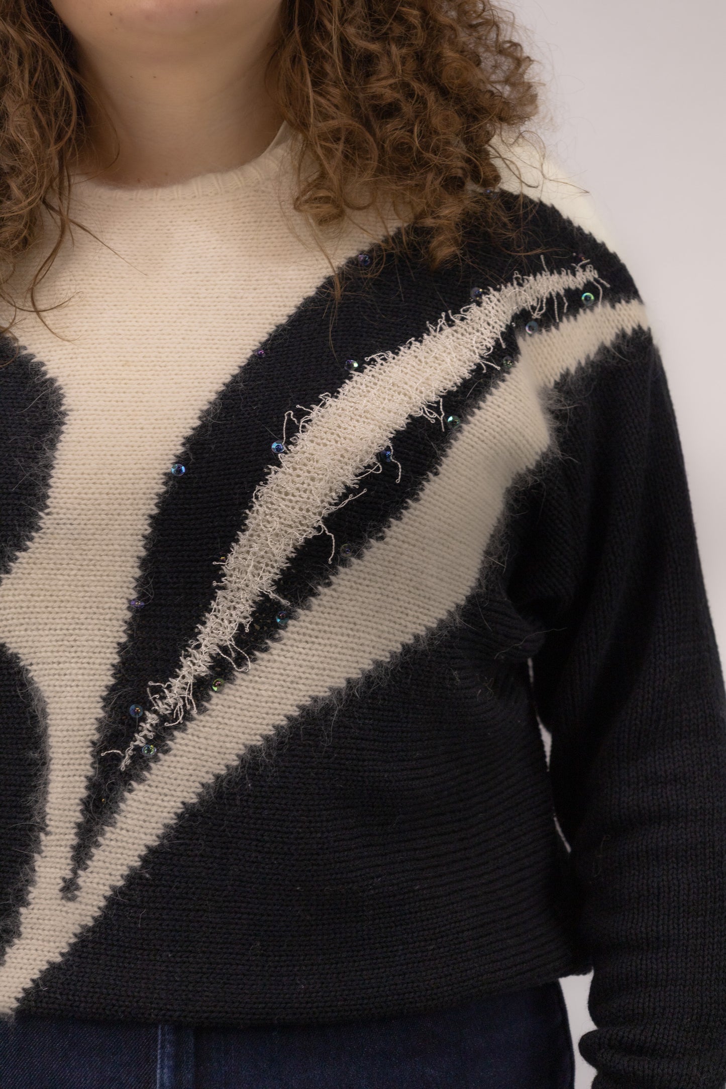 Detail van witte organische print met glitter en kralen op zwarte vintage trui