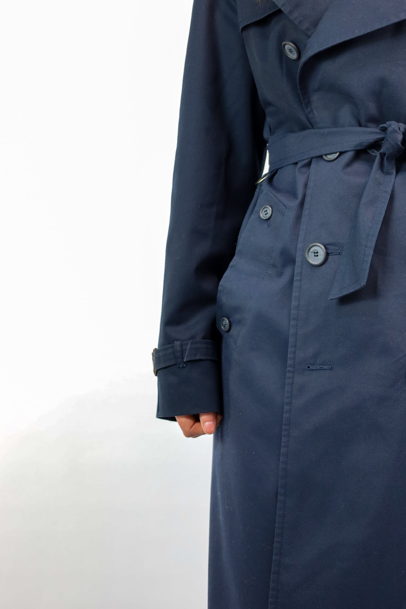 Detail van klassieke vintage trenchcoat in donkerblauw met steekzakken en knoopsluiting"