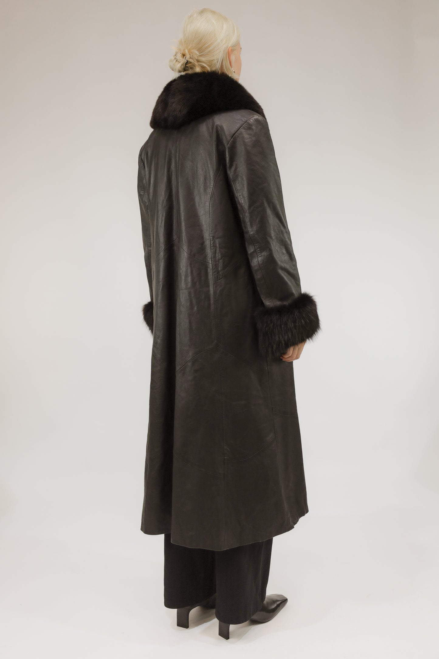 Model van achteren met lange zwarte leren vintage jas – licht uitlopend silhouet en glanzend leer.