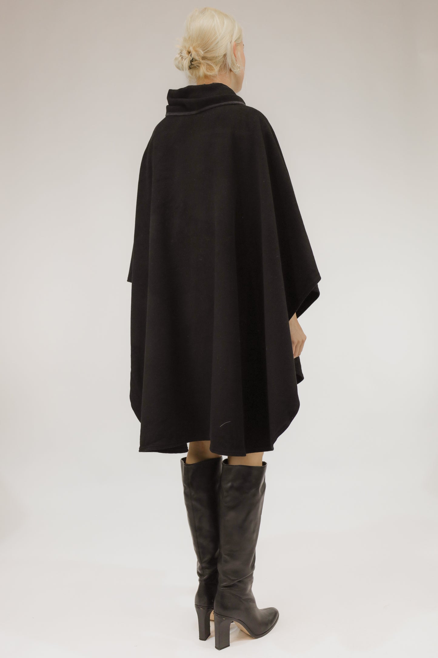 Achteraanzicht van model met ruim vallende zwarte poncho van wol.