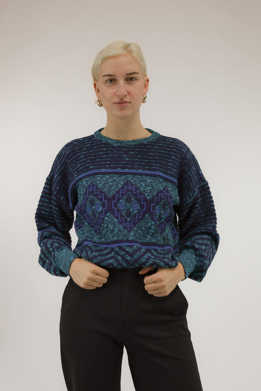 Model draagt stoere vintage trui met grafisch dessin in blauw- en groentinten – vooraanzicht.