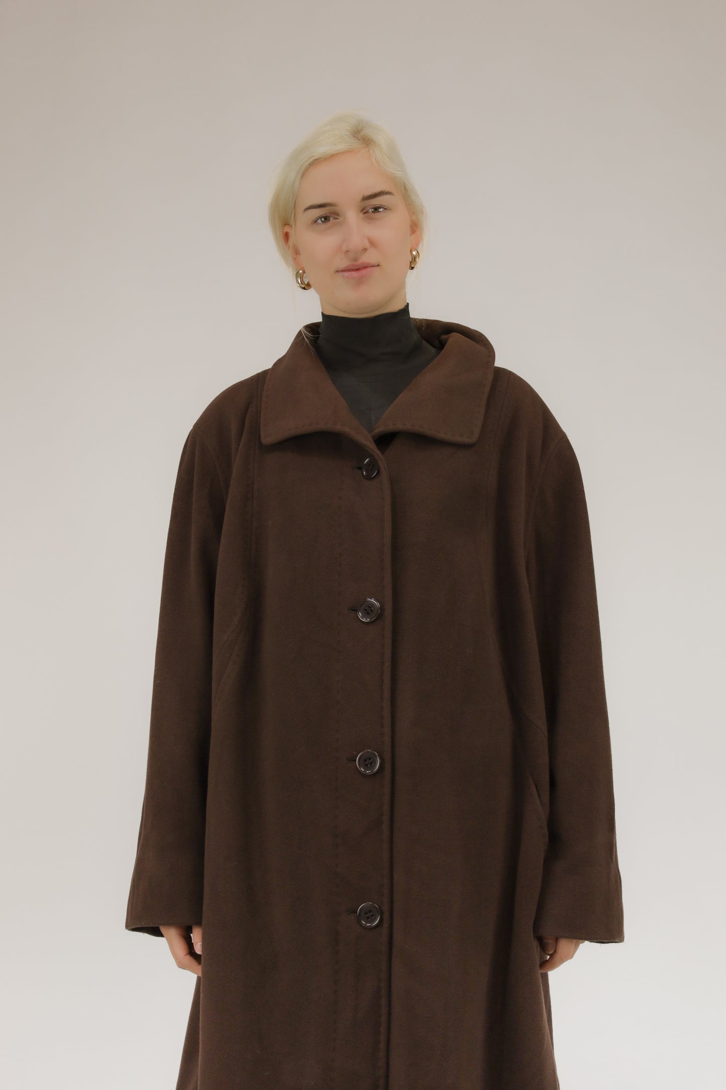 Model draagt bruine wollen mantel met afneembare kraag en capuchon met nepbont – vooraanzicht, A-lijn model.