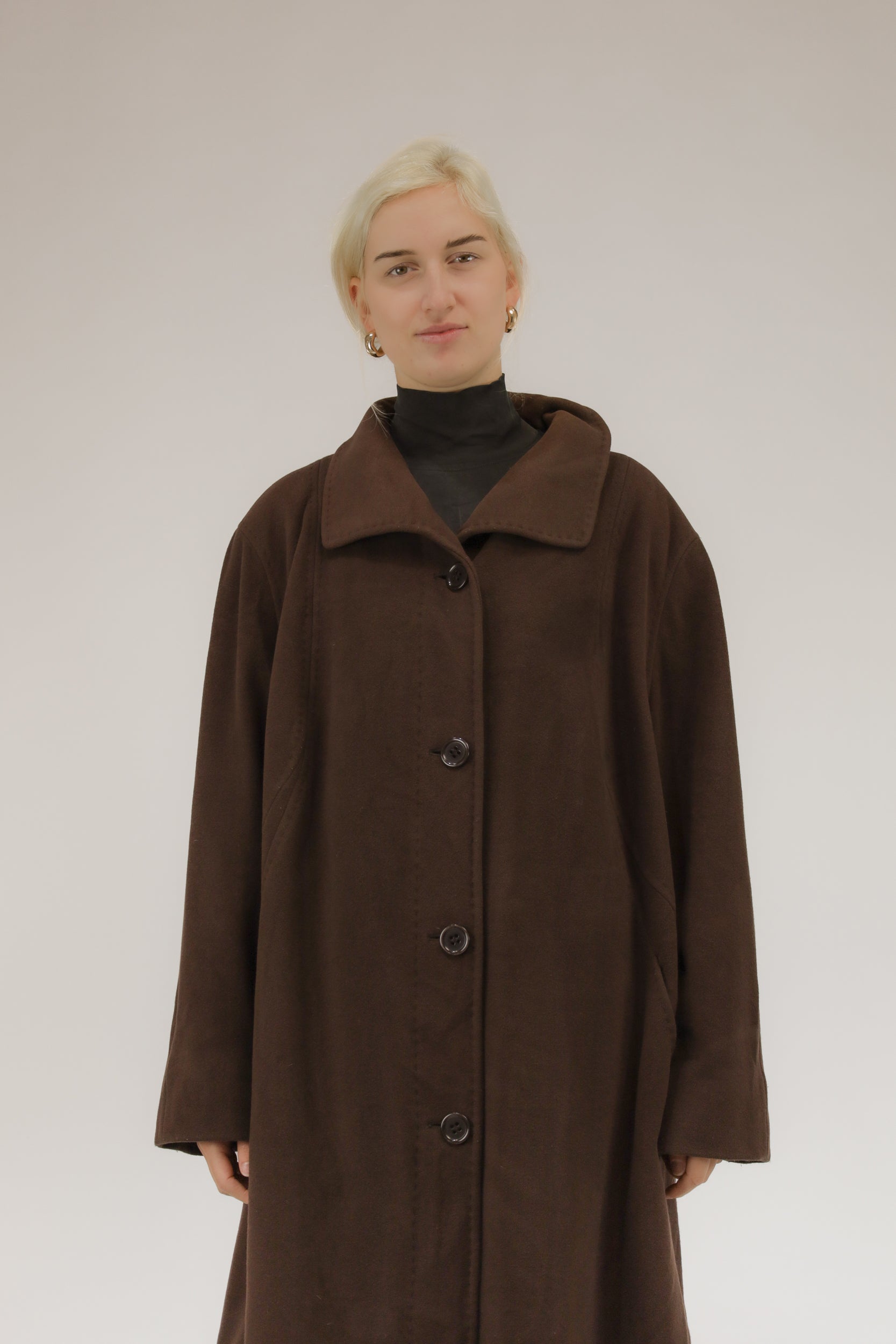 Model draagt bruine wollen mantel met afneembare kraag en capuchon met nepbont – vooraanzicht, A-lijn model.