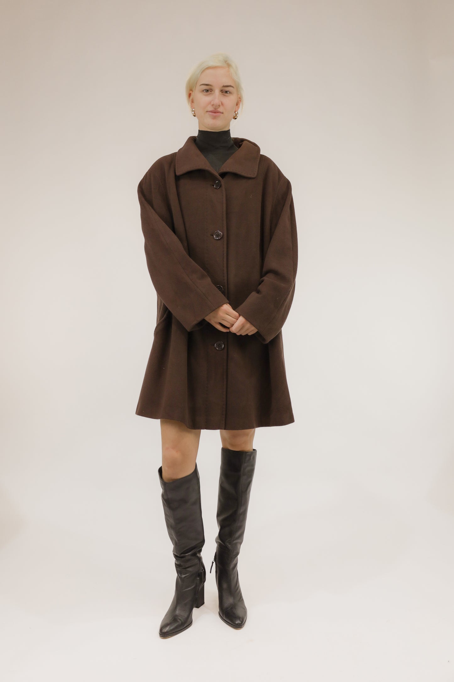 Model draagt bruine wollen mantel met afneembare kraag en capuchon met nepbont – vooraanzicht, A-lijn model.