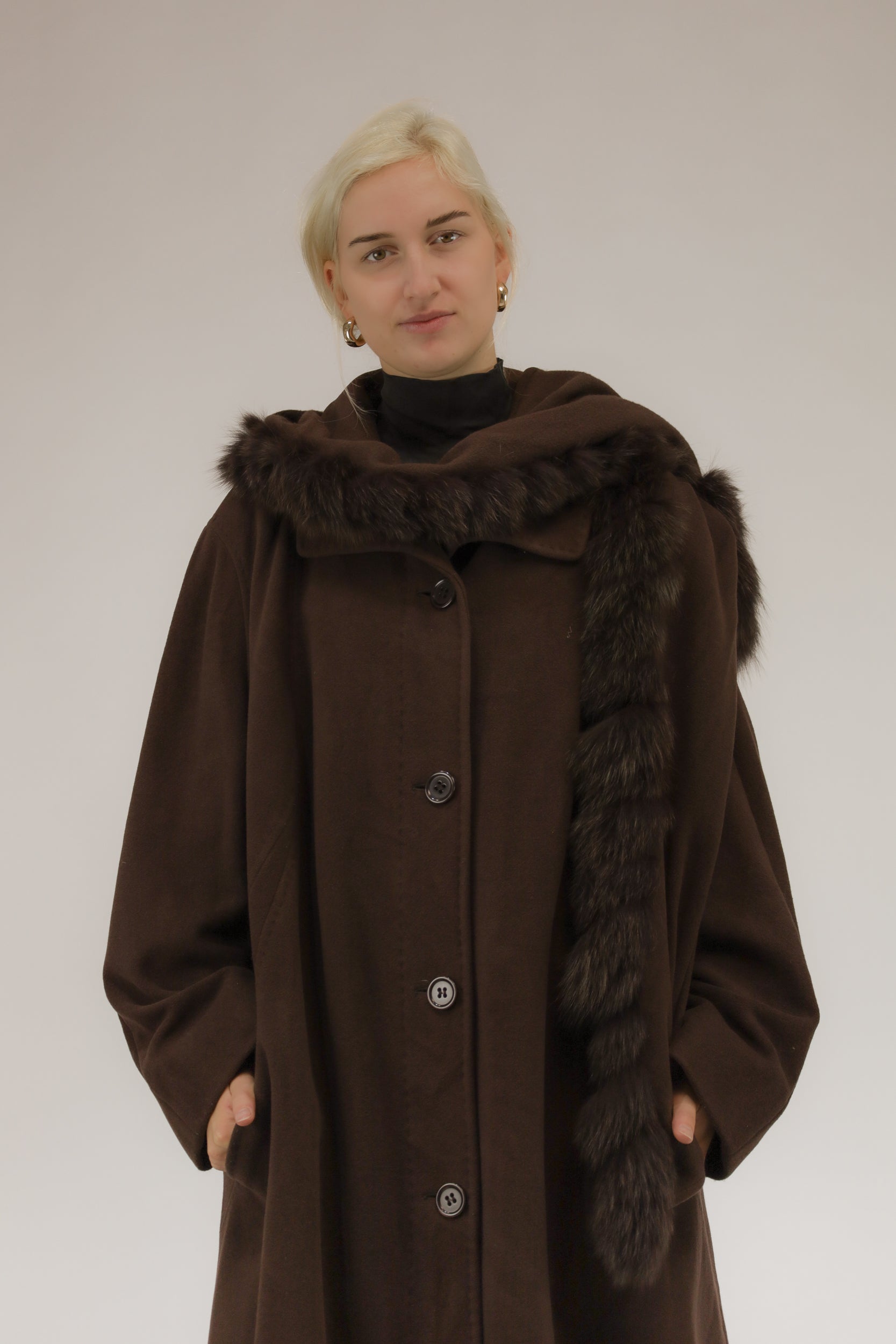 Model draagt bruine wollen mantel met afneembare kraag en capuchon met nepbont – vooraanzicht, A-lijn model.