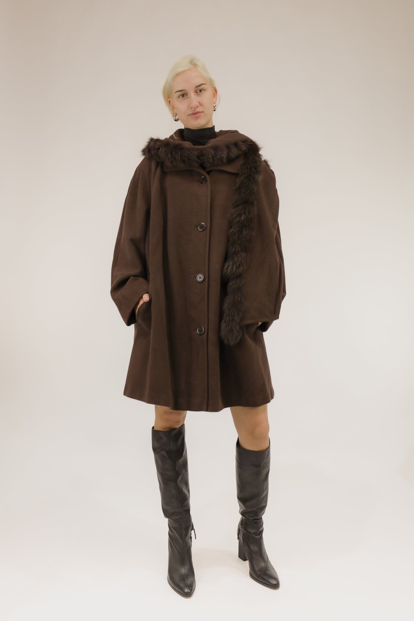 Model draagt bruine wollen mantel met afneembare kraag en capuchon met nepbont – vooraanzicht, A-lijn model.