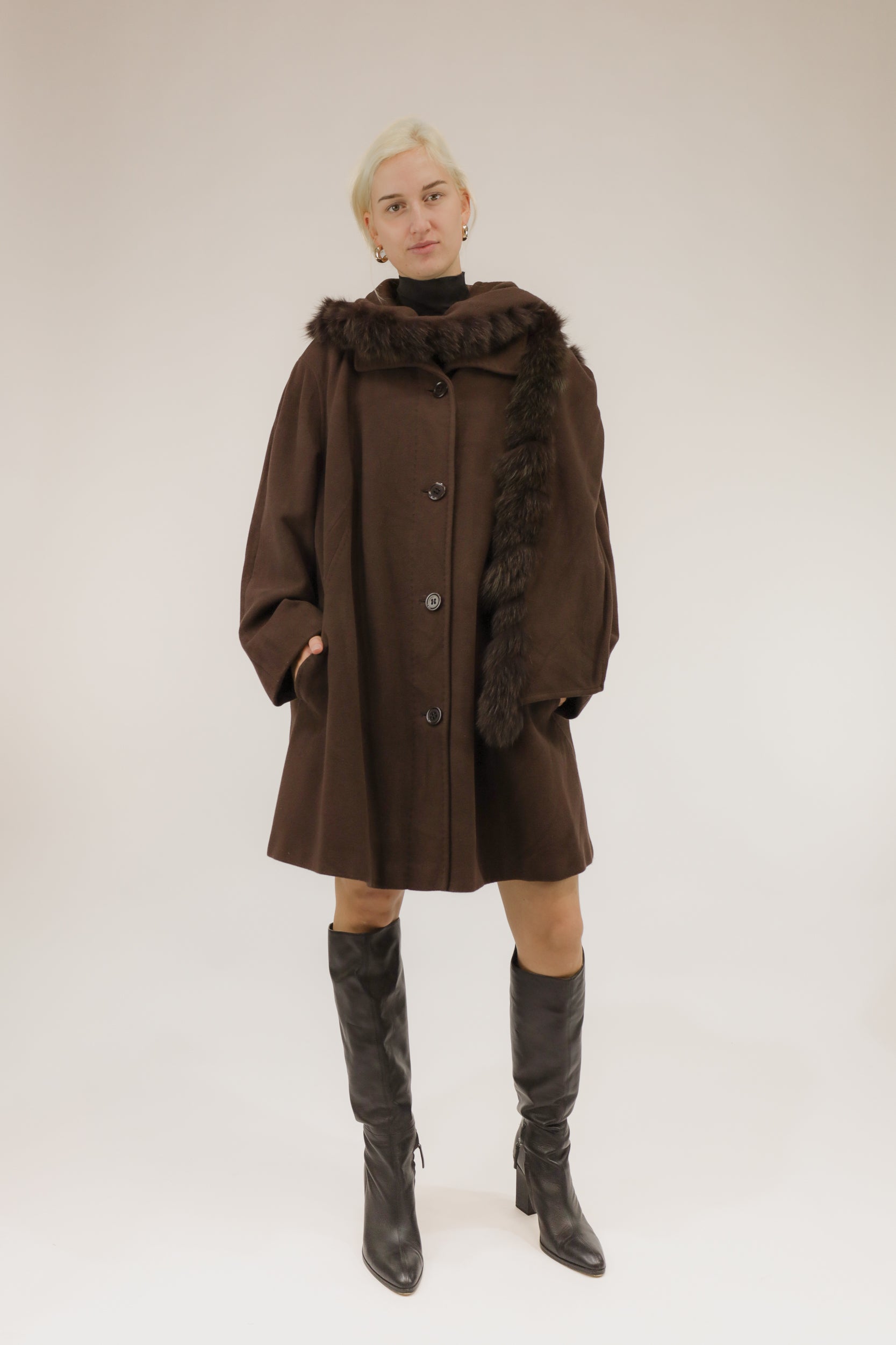 Model draagt bruine wollen mantel met afneembare kraag en capuchon met nepbont – vooraanzicht, A-lijn model.