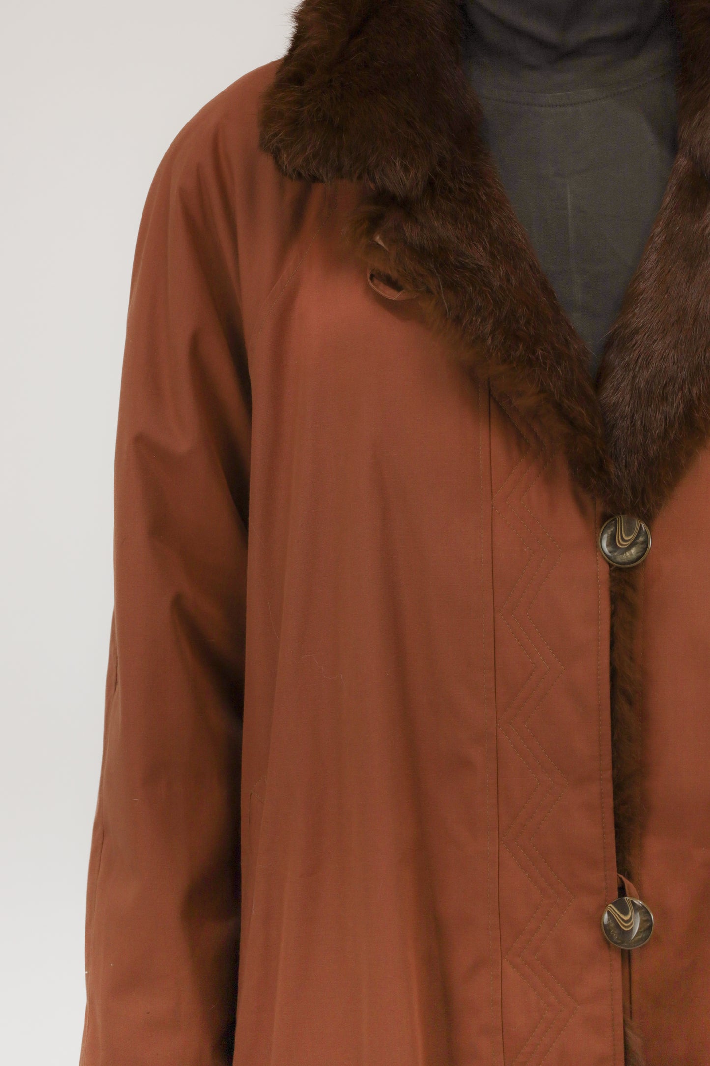 Close-up van model met vintage roestkleurige regenjas – detail van uitneembare faux fur voering en knoopsluiting.