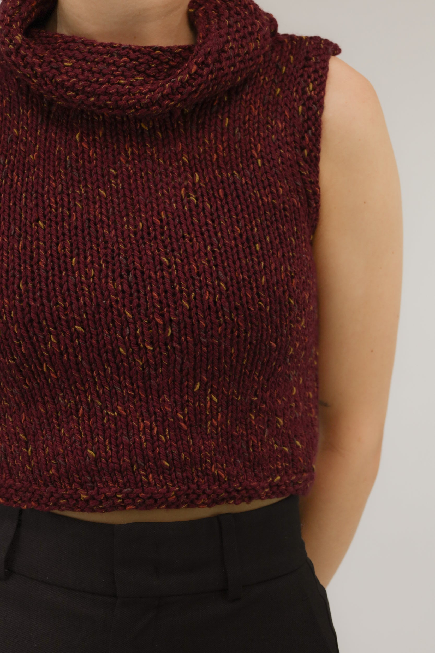 Detailopname van grof melange breisel en col van de mouwloze top.