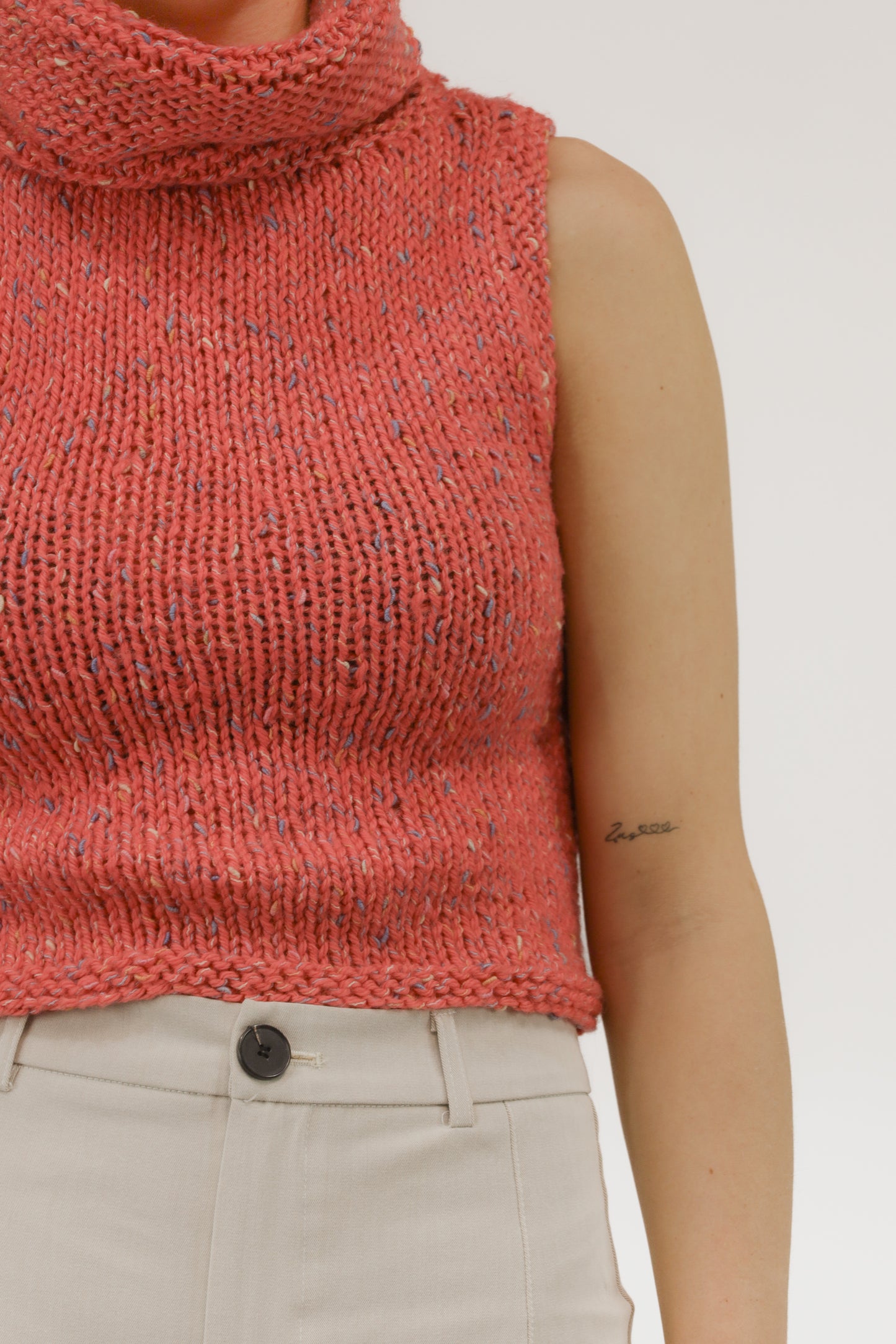 Detailopname van grof melange breisel en col van de mouwloze top.