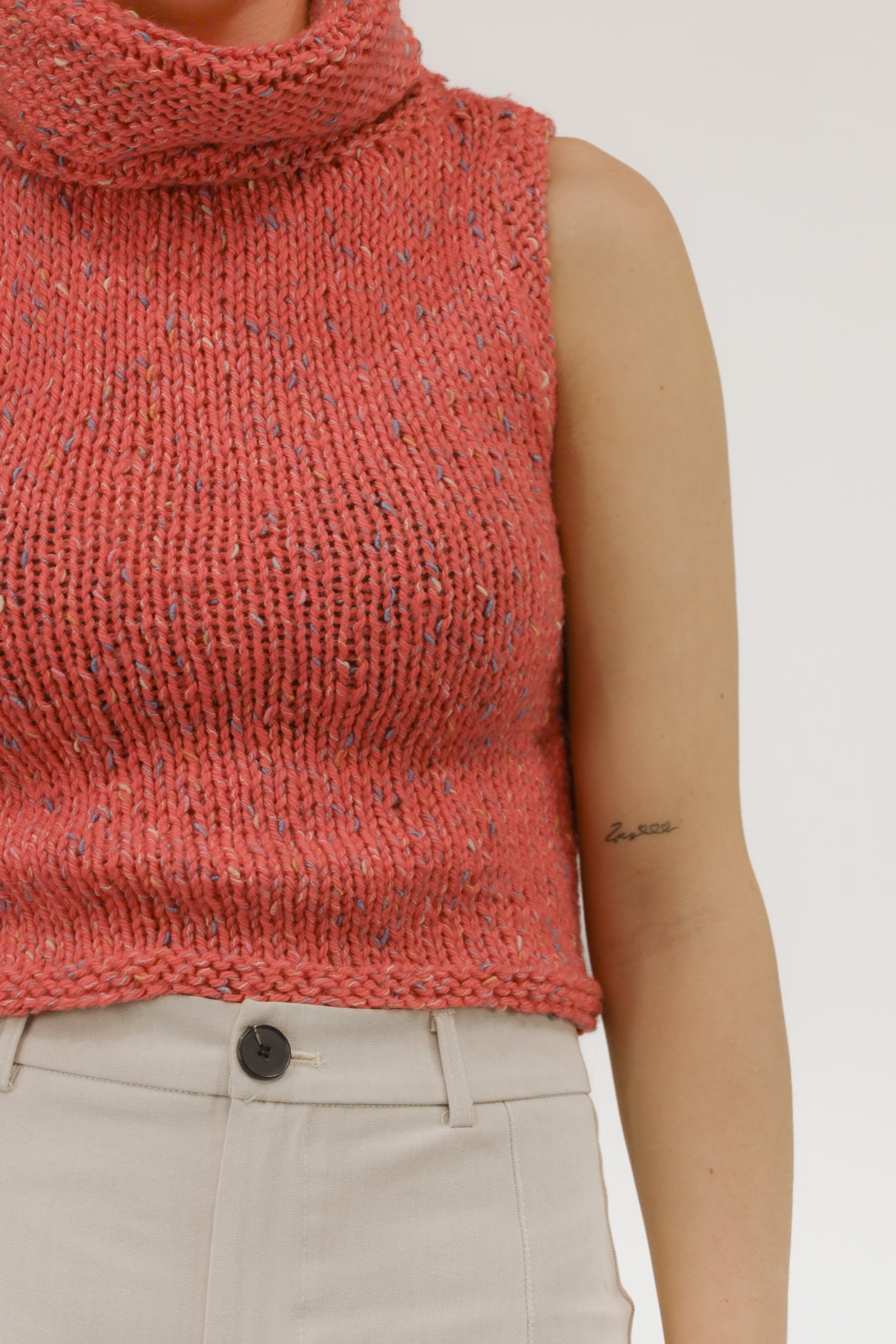 Detailopname van grof melange breisel en col van de mouwloze top.