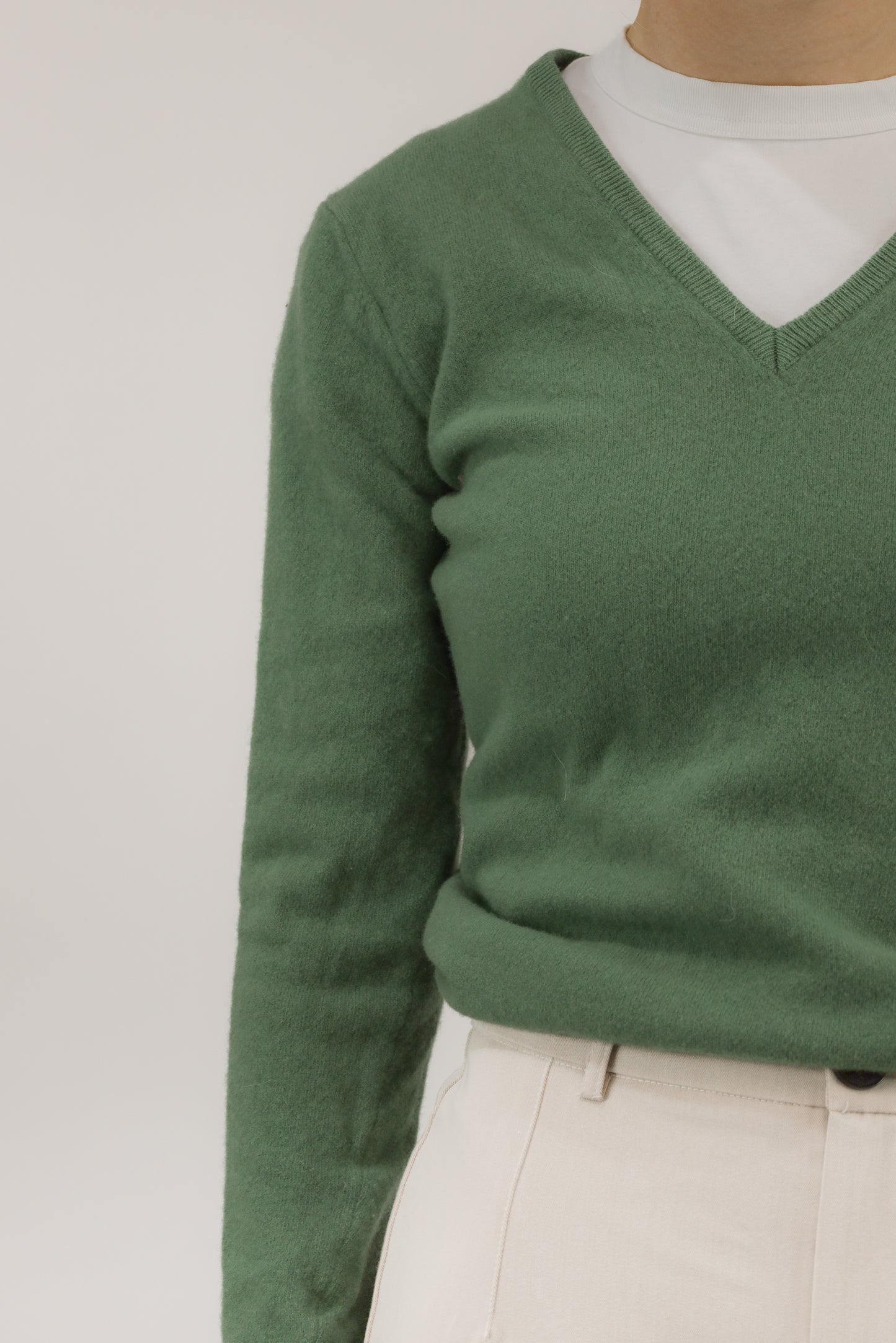 Close-up van model met groene wollen trui – detail van zachte wolkwaliteit en V-halslijn.