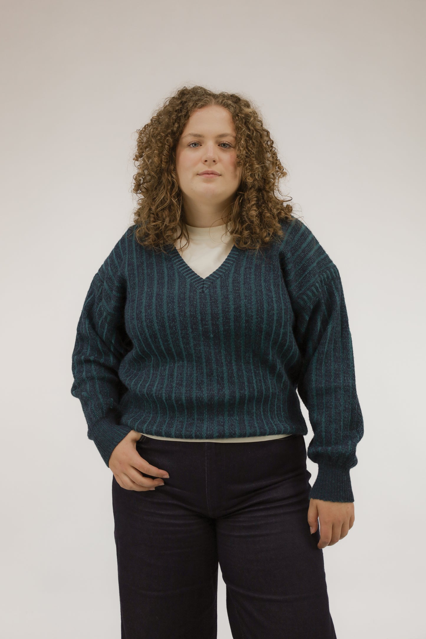 Vooraanzicht van model met vintage trui met streepdessin in groen- en blauwtinten en V-hals.