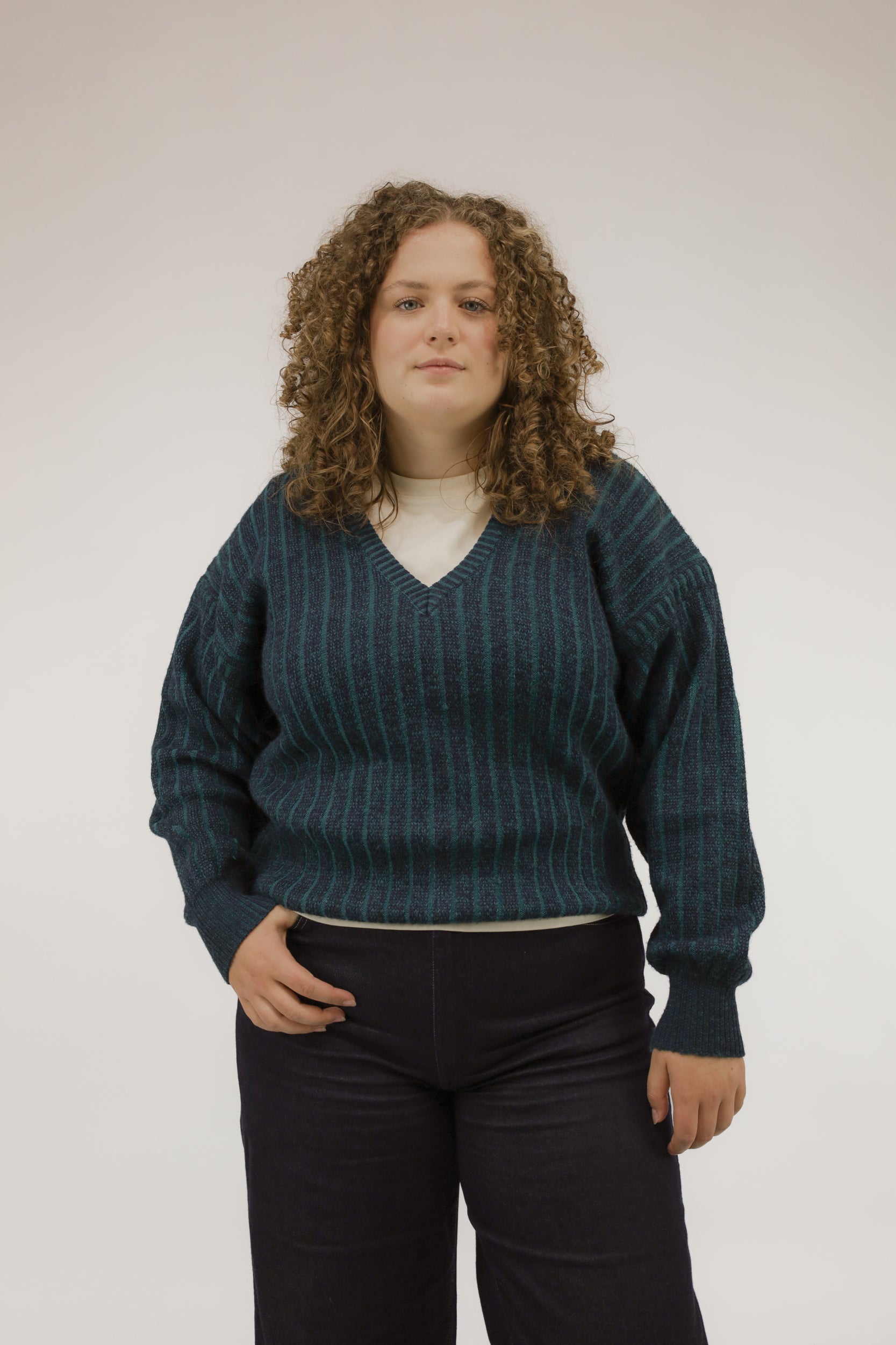 Vooraanzicht van model met vintage trui met streepdessin in groen- en blauwtinten en V-hals.