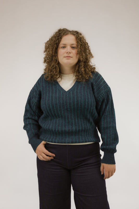 Vooraanzicht van model met vintage trui met streepdessin in groen- en blauwtinten en V-hals.