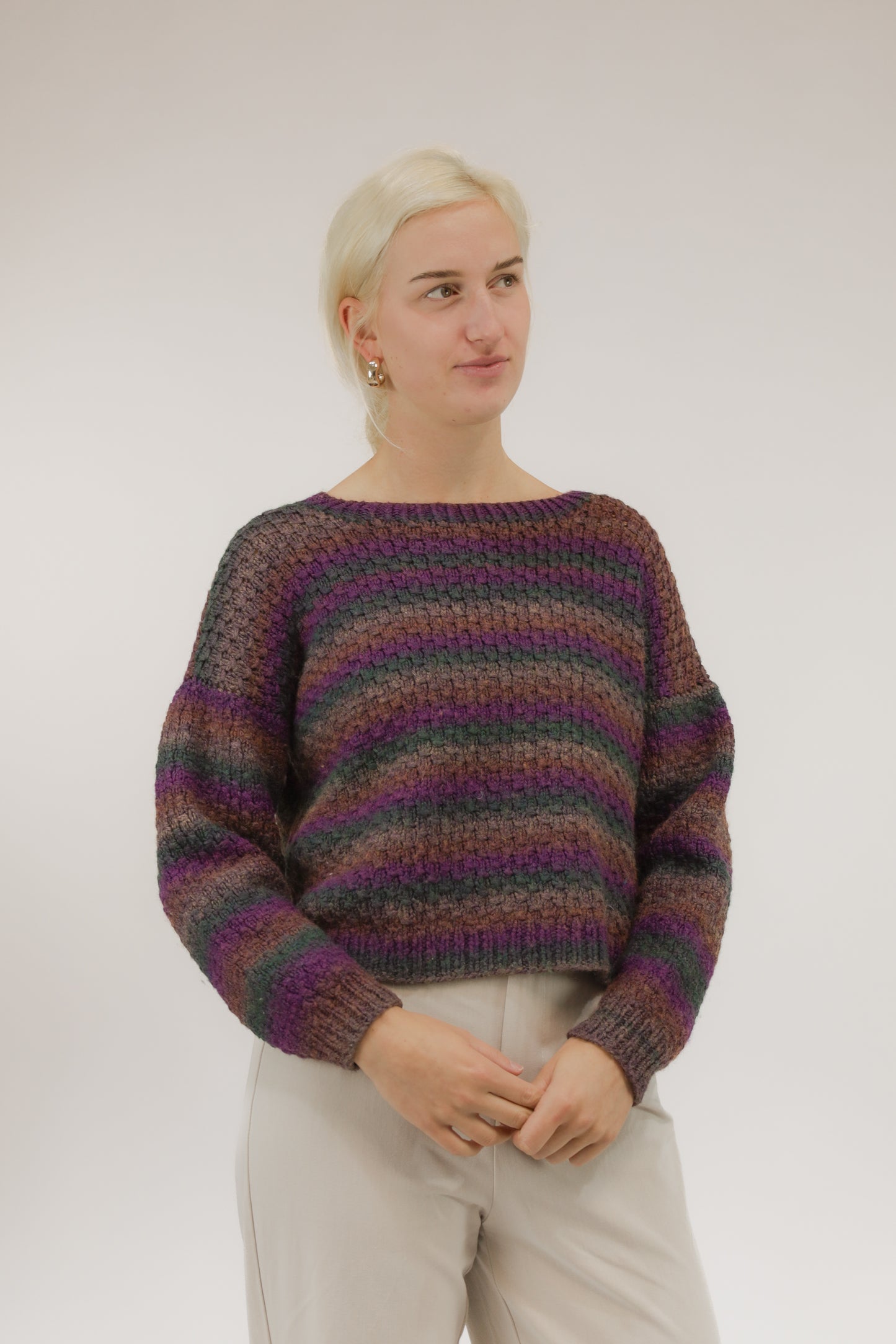 Model draagt grofgebreide vintage trui met streepdessin in paars, groen en bruin – cropped model, vooraanzicht.