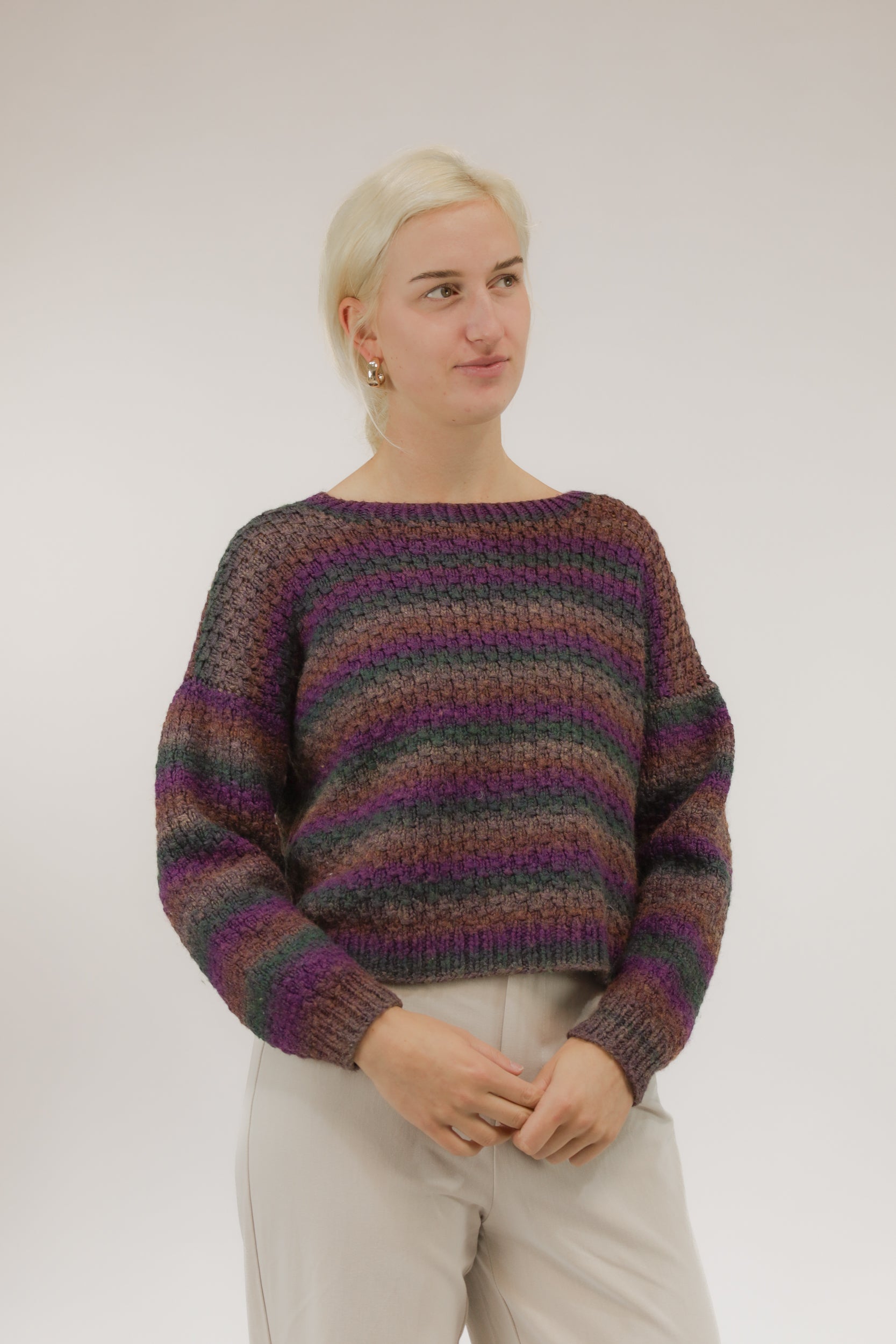Model draagt grofgebreide vintage trui met streepdessin in paars, groen en bruin – cropped model, vooraanzicht.