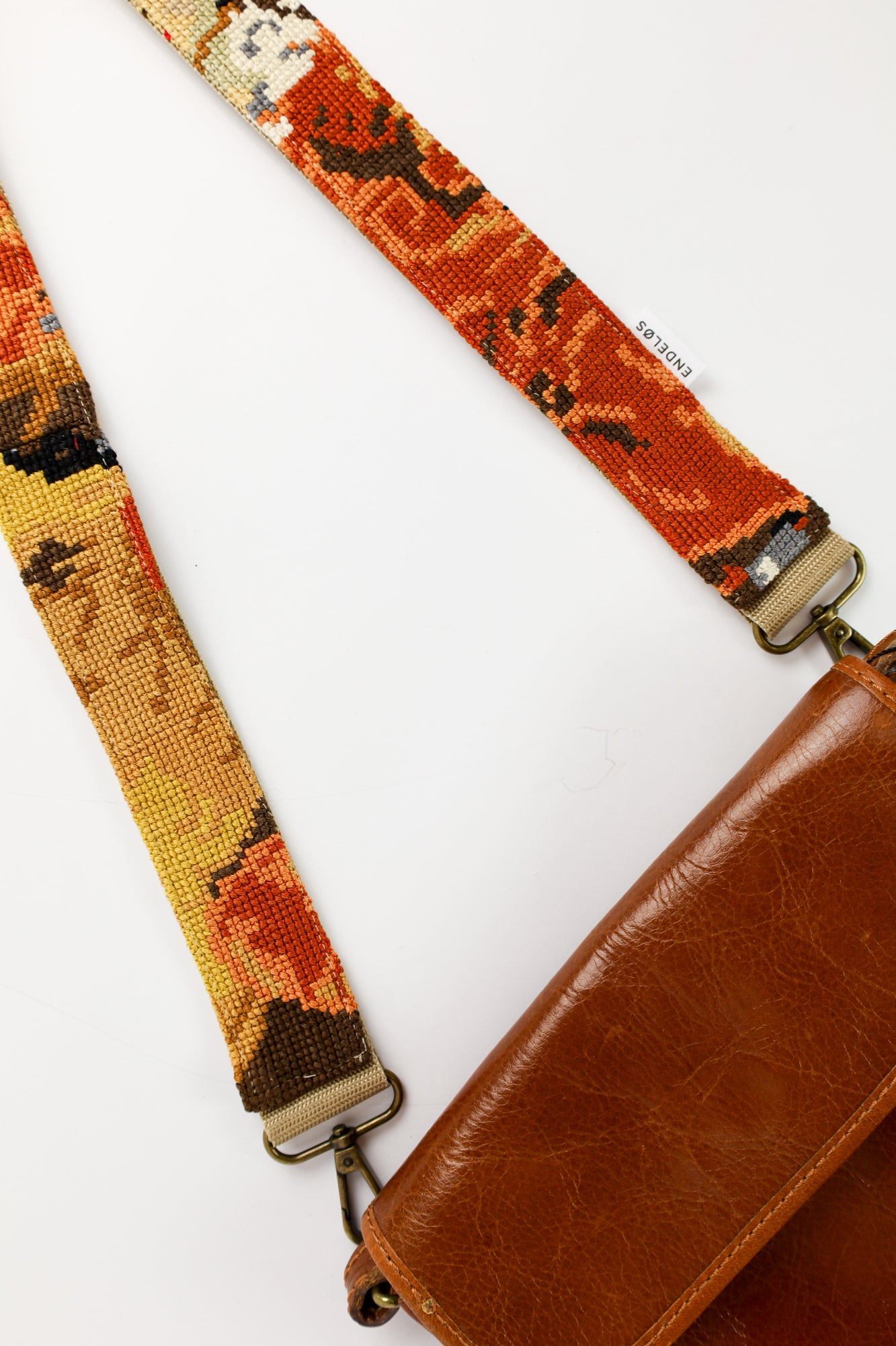Handgemaakte strap van het borduurwerk The Red Boy, uitgevoerd in warme rood- en oranjetinten, perfect voor tas, telefoon of camera.