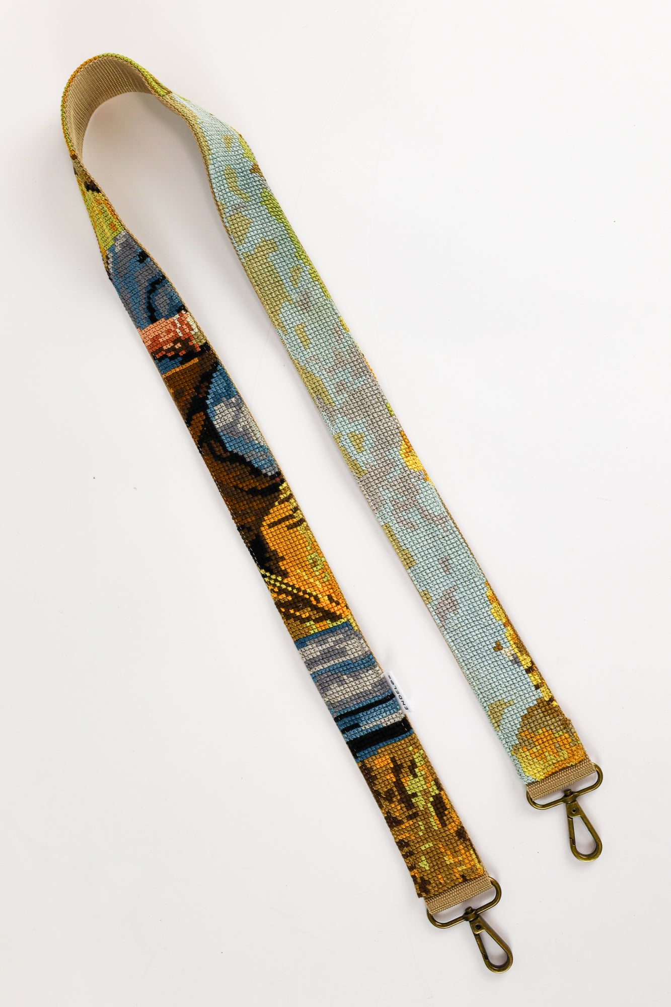 Strap made from a painting illustrating working farmers, with a mix of yellow, blue, green, brown, and a small pink accent, a unique addition to your bag, phone, or camera.