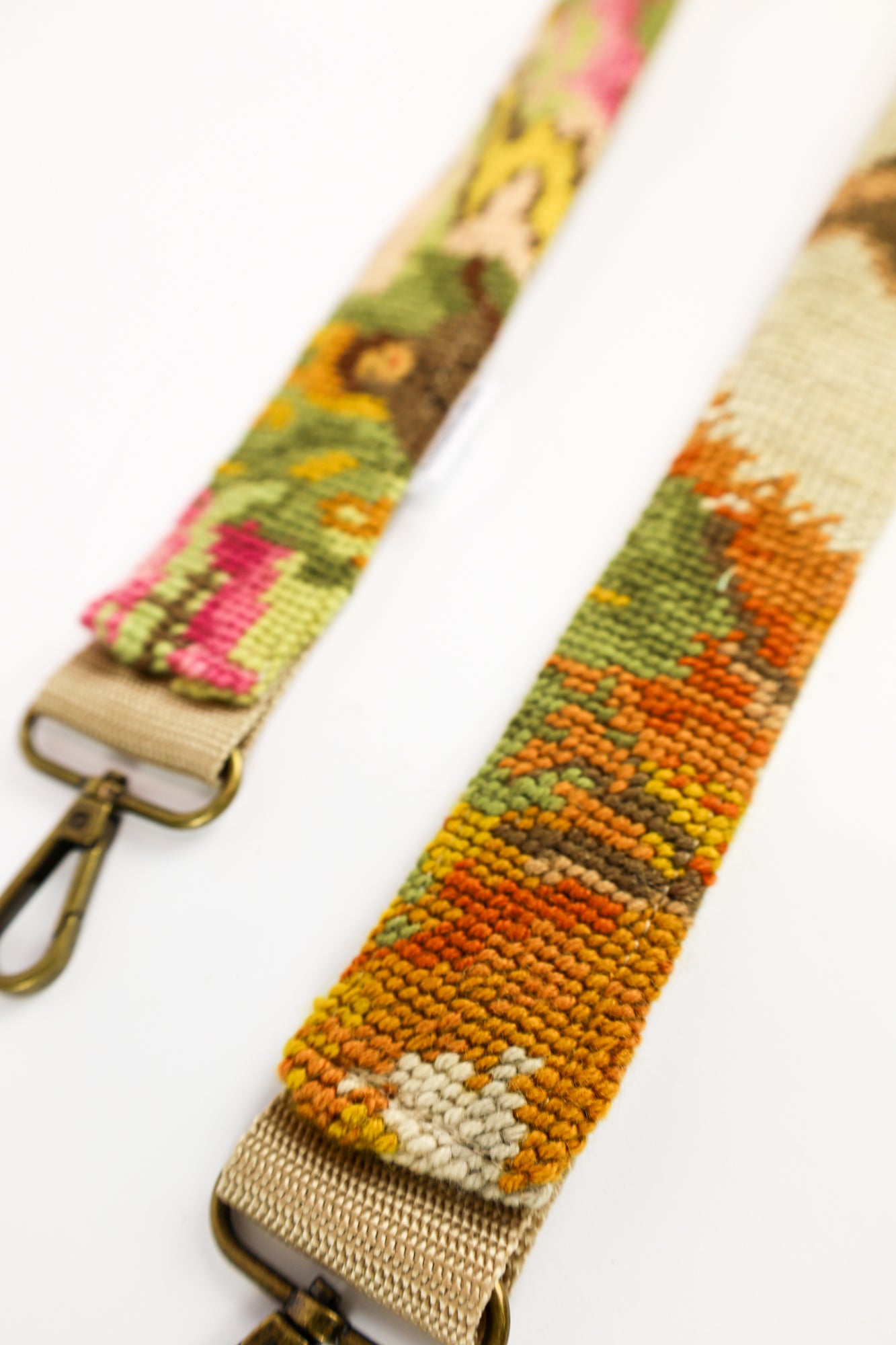 Close-up van de strap met geborduurd schilderij van een boerderij en schapenhoeder op een bloemig veld.