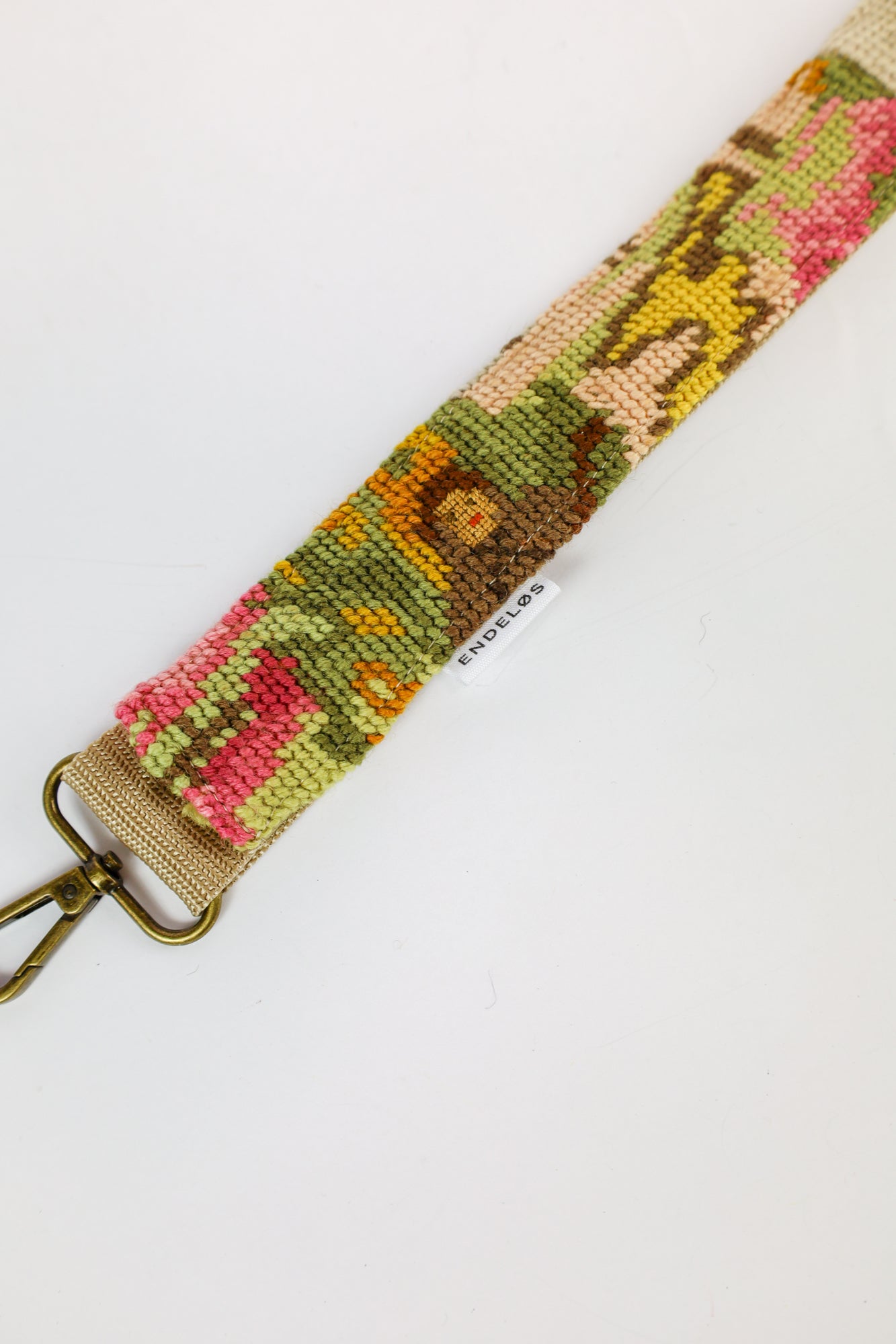 Strap van hergebruikte materialen met geborduurd schilderij van een schapenhoeder op een veld vol bloemen.