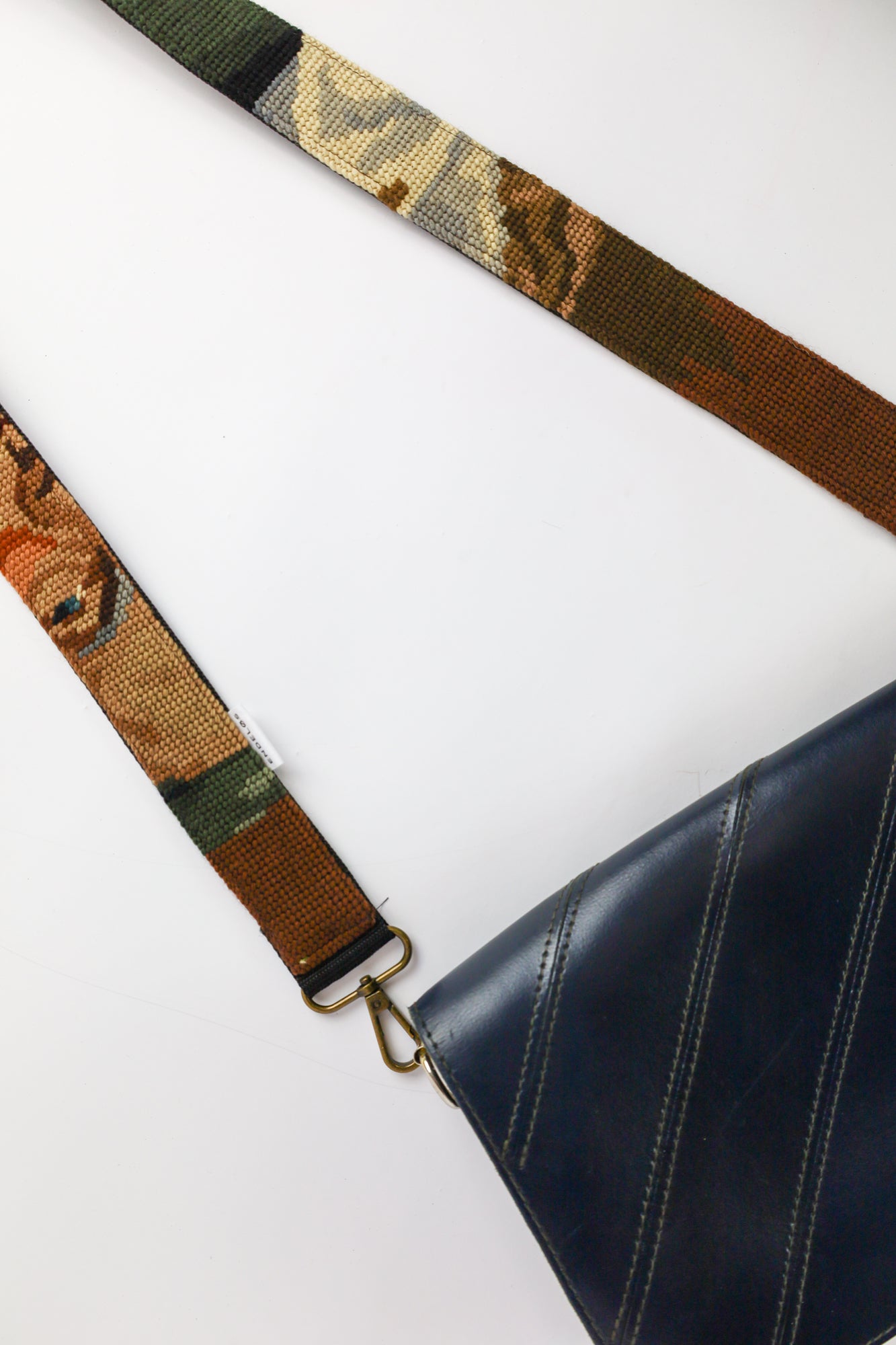 Handgemaakte strap van geborduurd schilderij met een drinkende man, in donkere tinten groen, zwart en bruin, een unieke toevoeging voor je tas of camera.