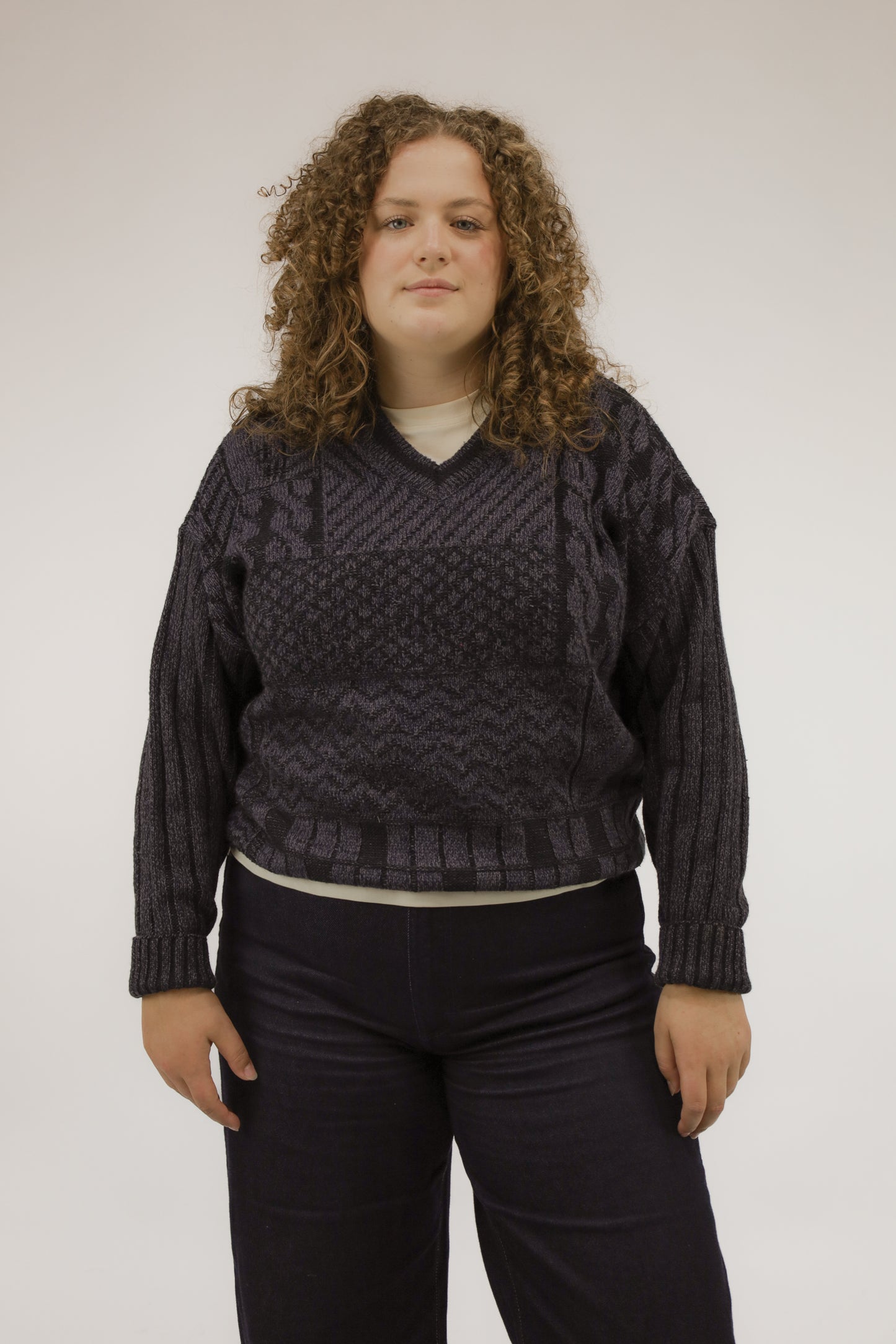 Model draagt oversized vintage trui met V-hals in paars en donkerblauw – grafisch patroon van blokken, strepen en golven – vooraanzicht.