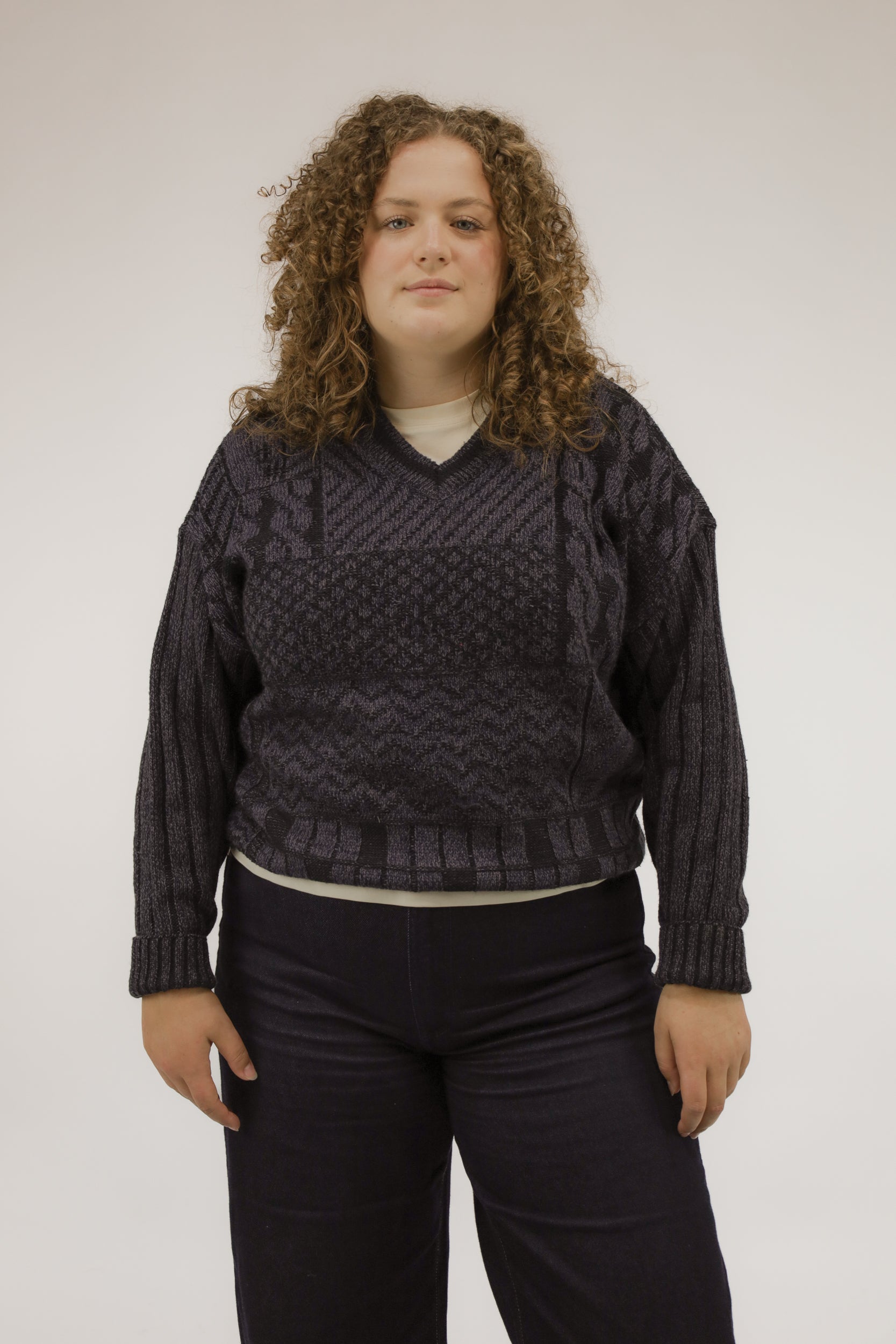 Model draagt oversized vintage trui met V-hals in paars en donkerblauw – grafisch patroon van blokken, strepen en golven – vooraanzicht.