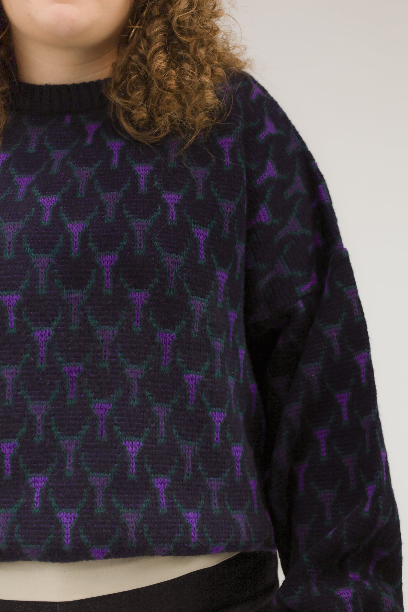 Close-up van model met donkerblauwe vintage trui – detail van ingebreid grafisch patroon in paars en groen.