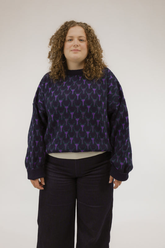 Model draagt donkerblauwe vintage trui met grafisch ingebreid dessin in paars en groen – vooraanzicht.