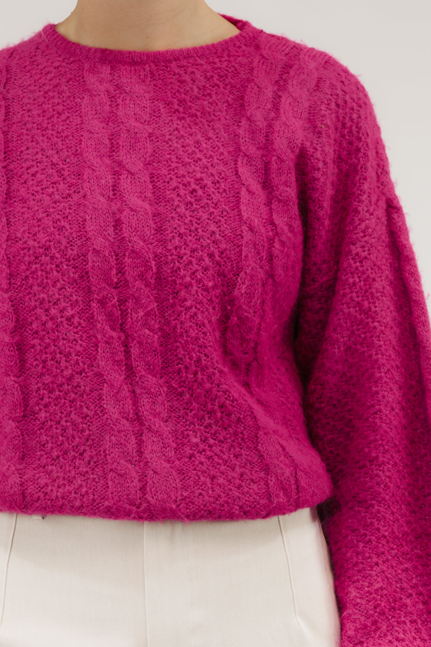 Close-up van model met zuurstokroze vintage trui – detail van kabelstructuur en dunne breikwaliteit.