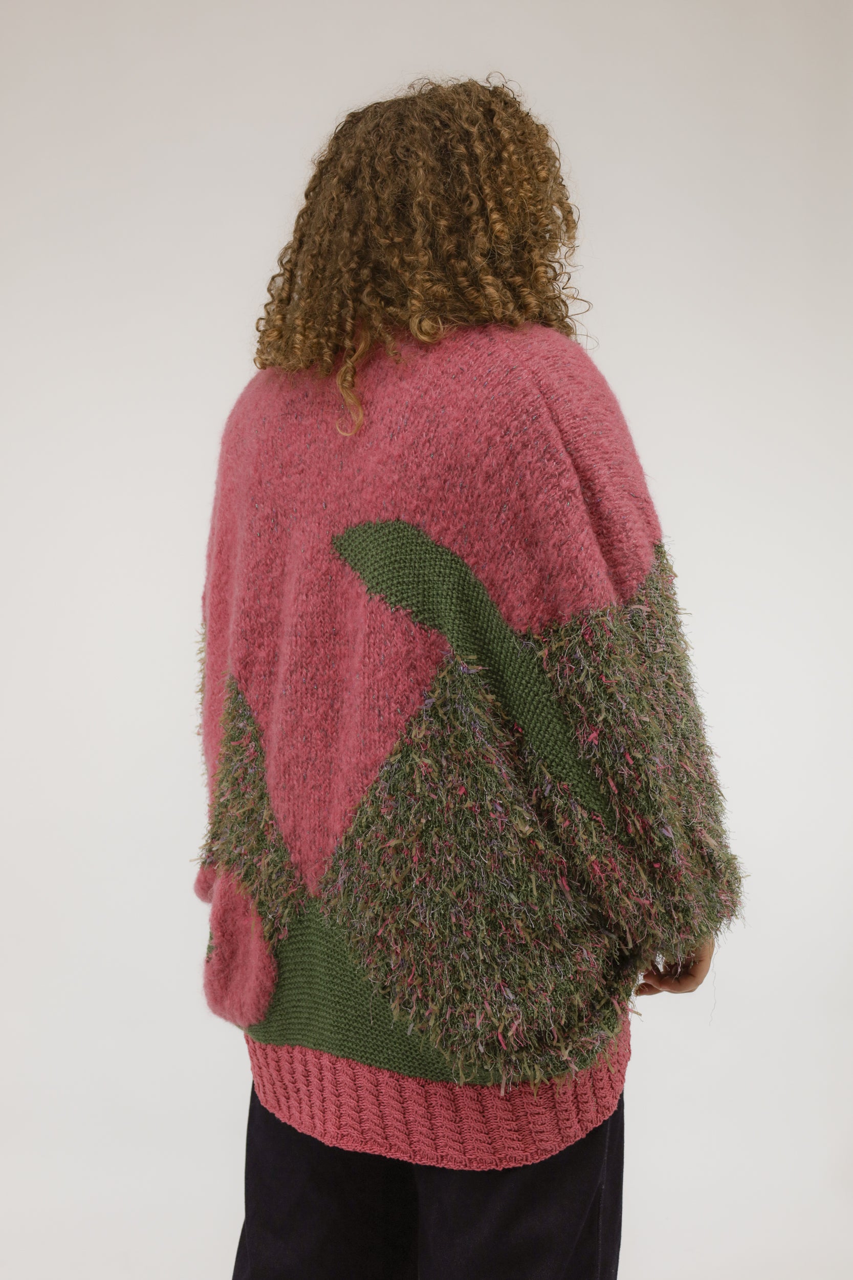 Model van achteren met oversized mosgroen vintage vest met zuurstokroze details en gemengde breisels.