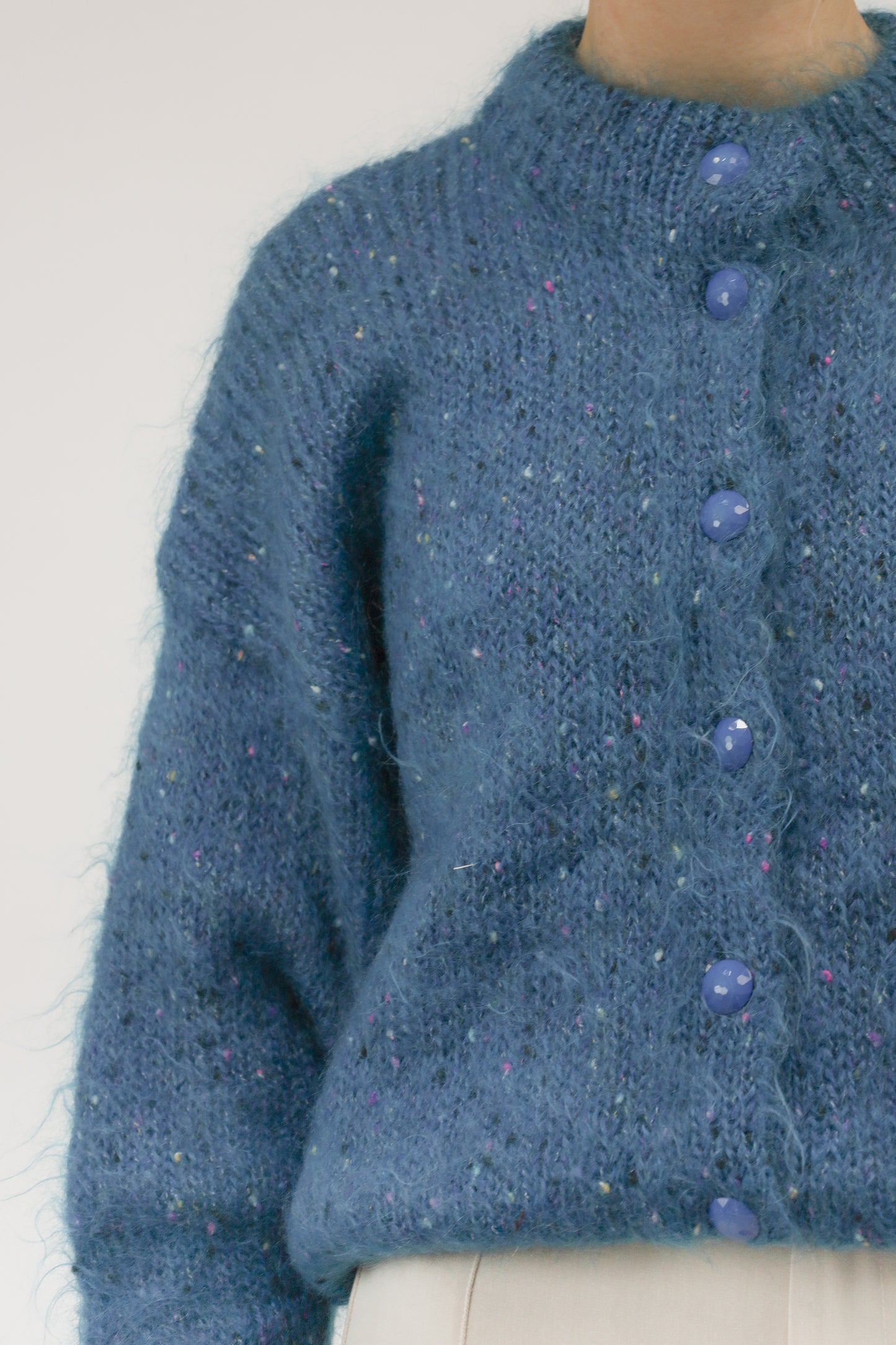 Close-up van model met vintage handgebreid turquoise vest met ingeweven bolletjes en grote kraalknoop.