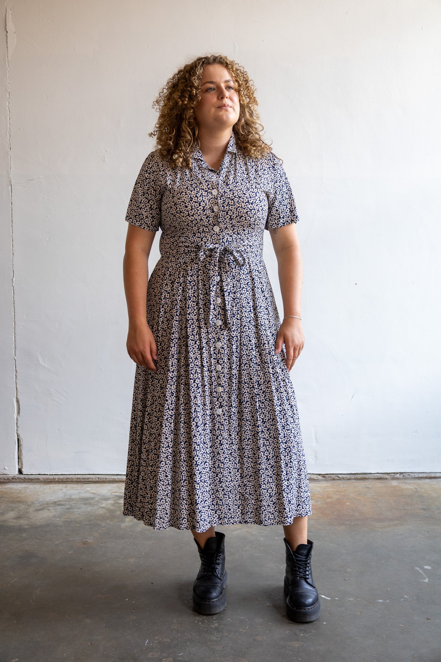 Vintage donkerblauwe jurk met wit-beige bloemenprint, knoopsluiting en strikceintuur.