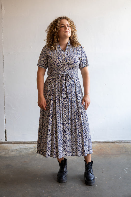 Vintage donkerblauwe jurk met wit-beige bloemenprint, knoopsluiting en strikceintuur.