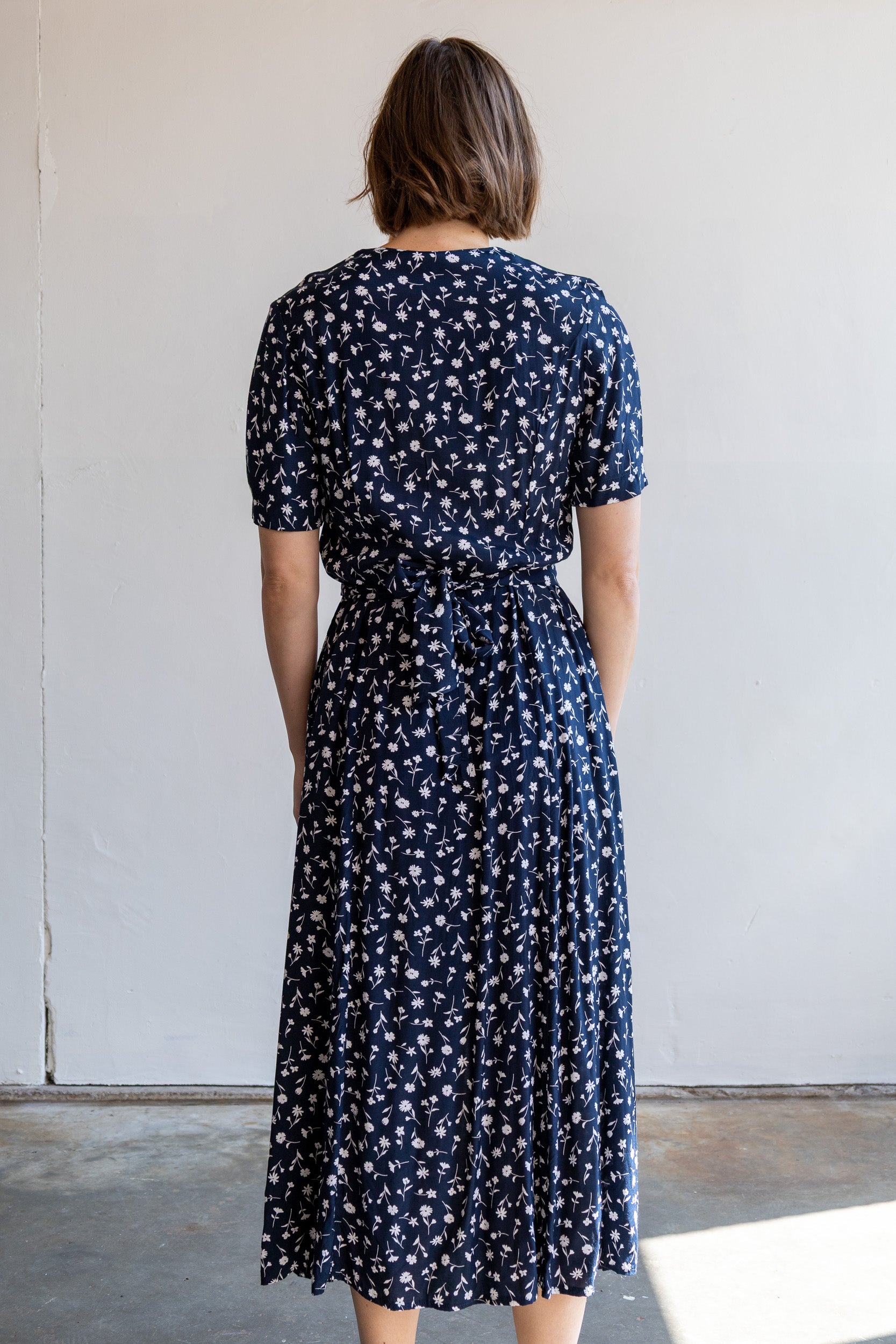Achterzijde van de vintage donkerblauwe jurk met strikceintuur en splitten.