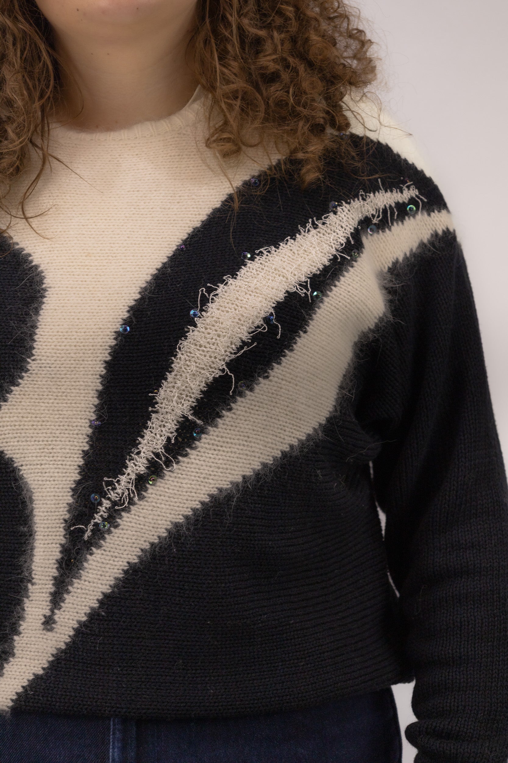Detail van witte organische print met glitter en kralen op zwarte vintage trui