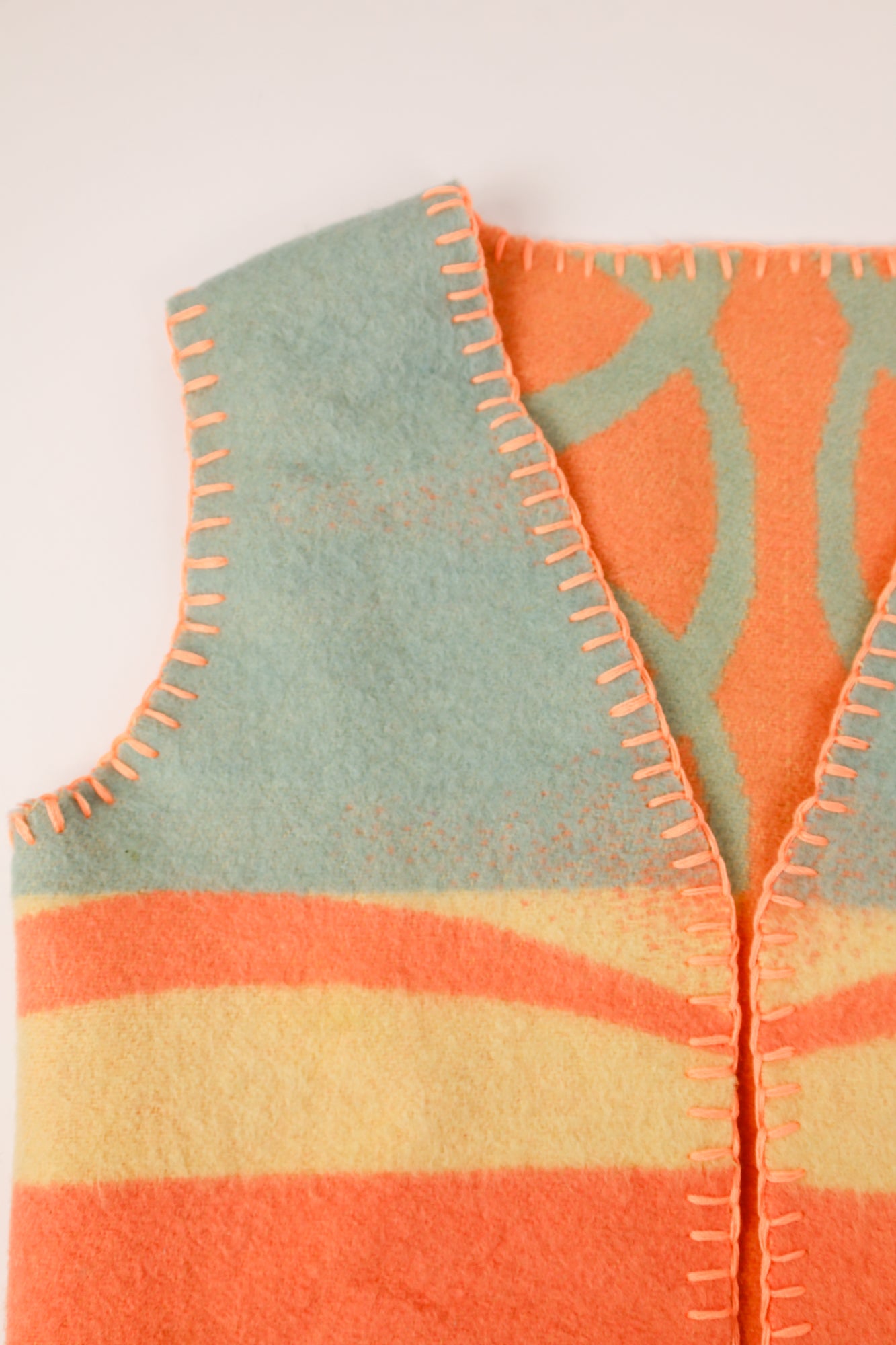 Close-up of the soft pastel wool texture with bold orange thread for contrast.