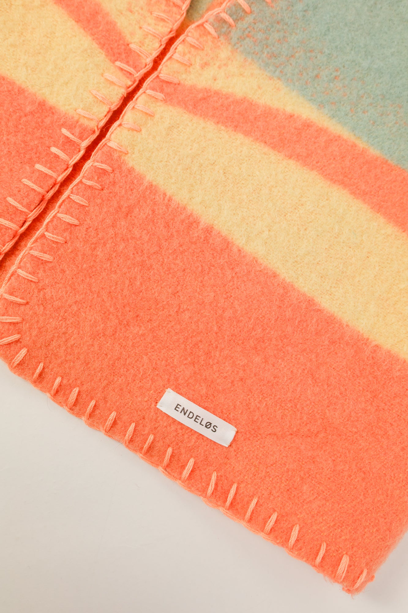 Close-up of the soft pastel wool texture with bold orange thread for contrast.