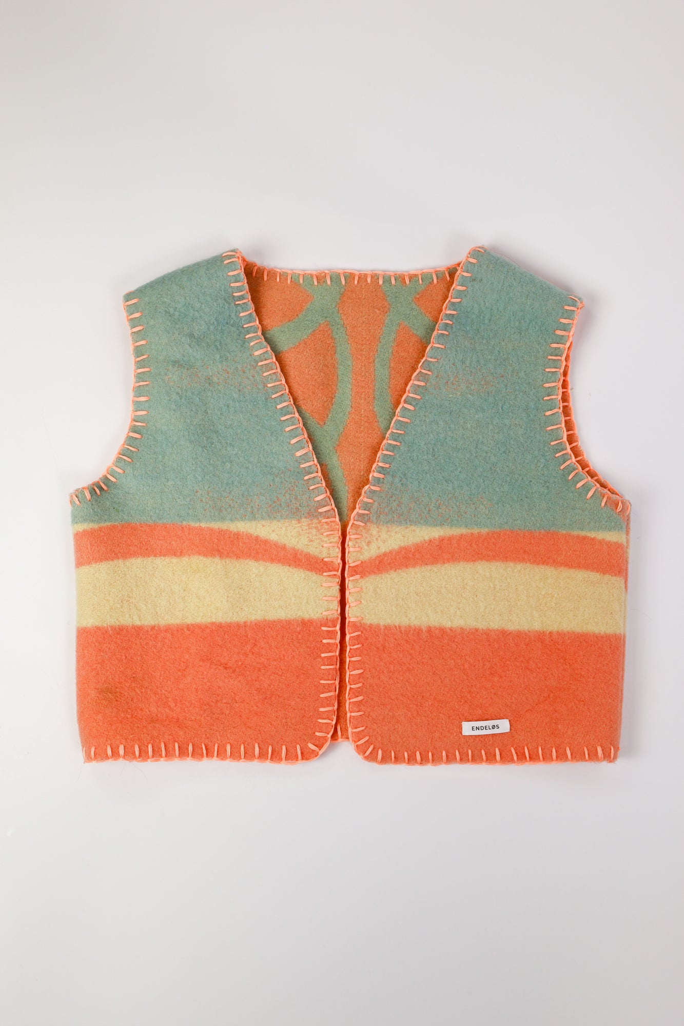 Front view of the handmade oversized vest, featuring pastel wool fabric with bright orange stitching.