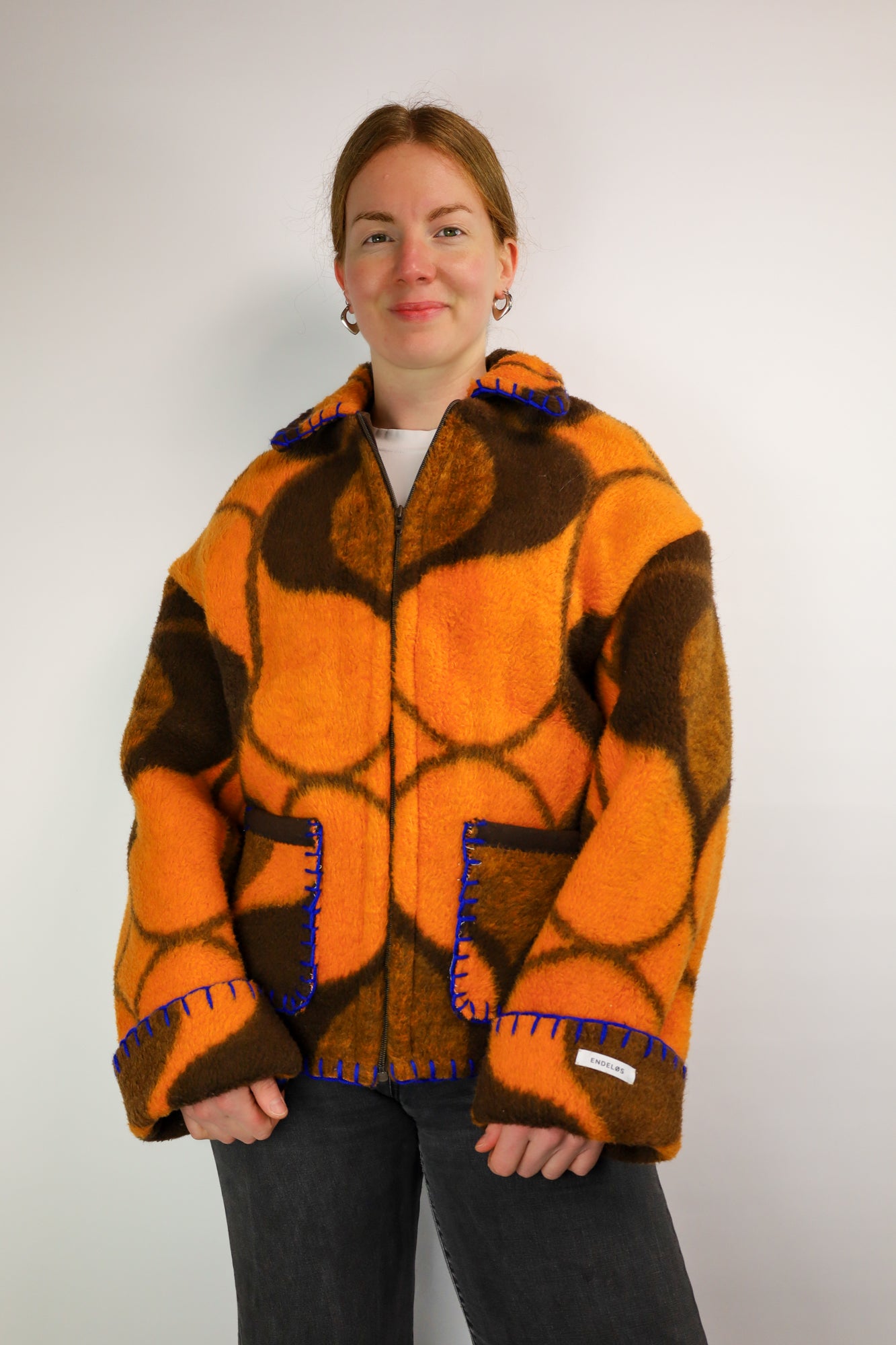 Front view of the upcycled coat featuring a bold brown and orange retro print with bright blue stitching.