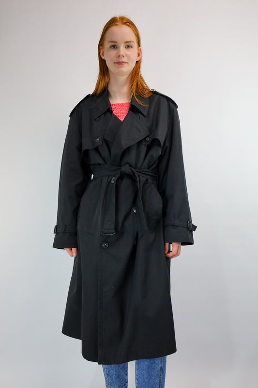 Voorkant van een klassieke zwarte vintage trenchcoat met ceintuur en epauletten.