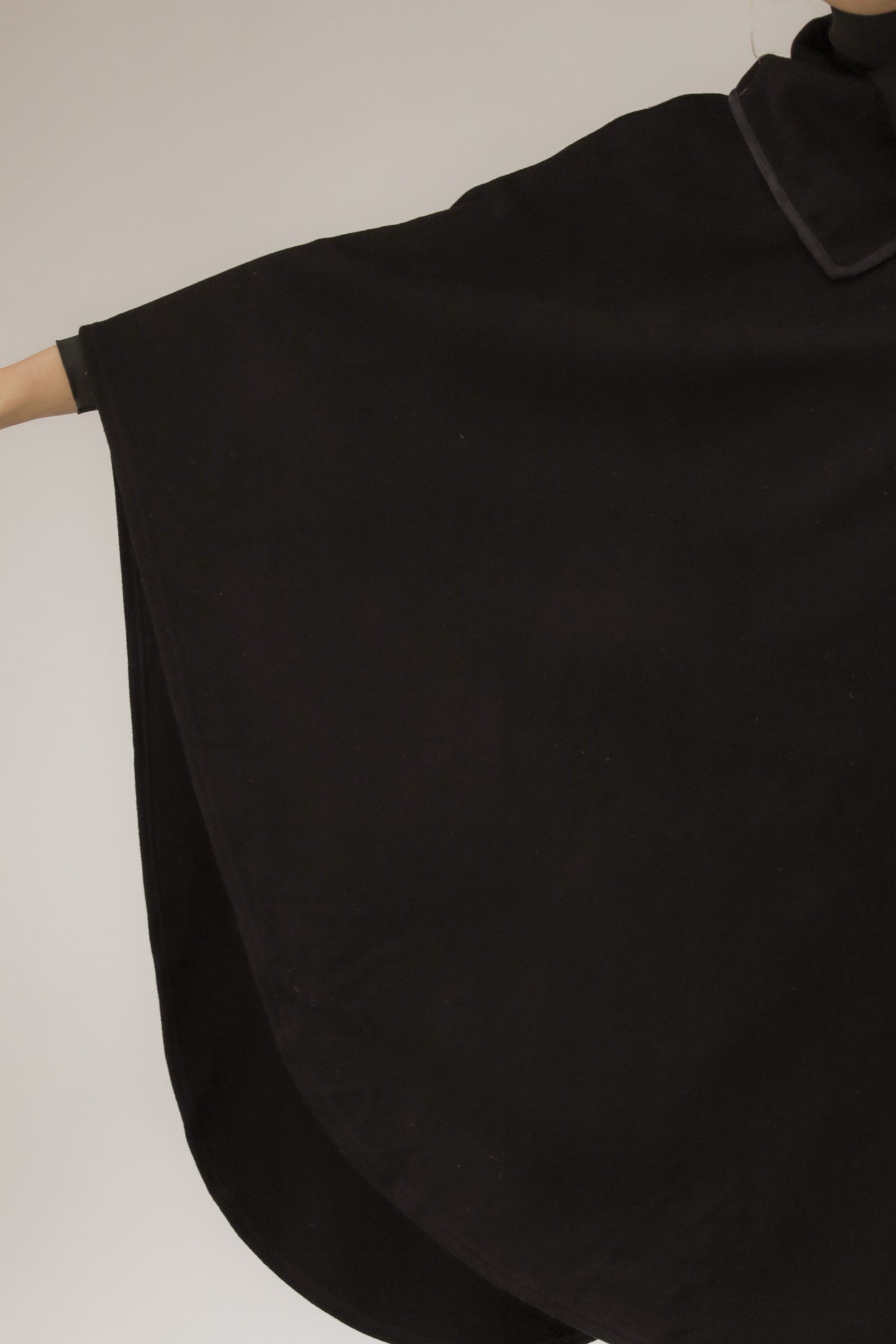 Detailopname van zwarte poncho, close-up van biasband en wolstructuur.